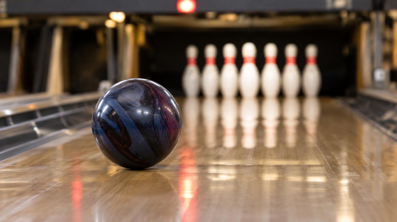 A bowling ball rolling down a polished lane toward a set of pins.