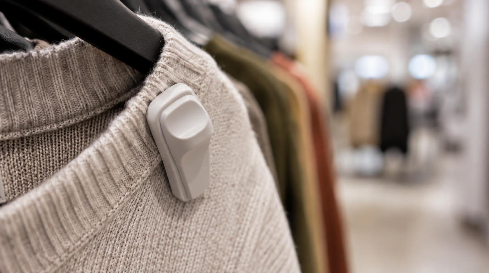 A hard plastic security tag clipped to a garment hanging on a retail store rack.