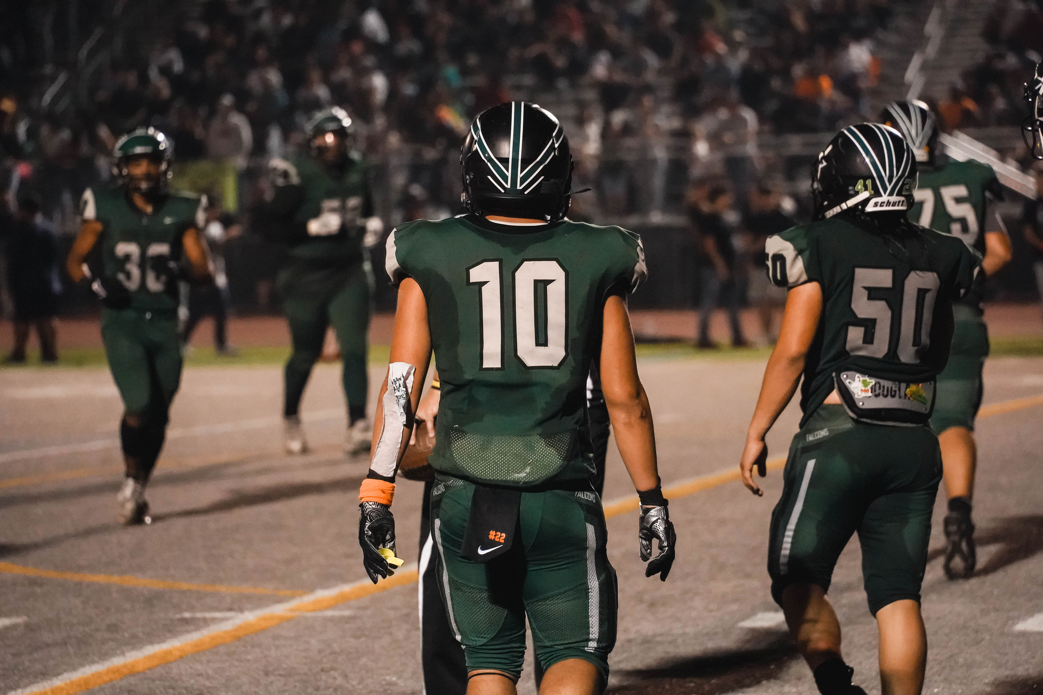 High school football players in green uniforms on a lit field at night.