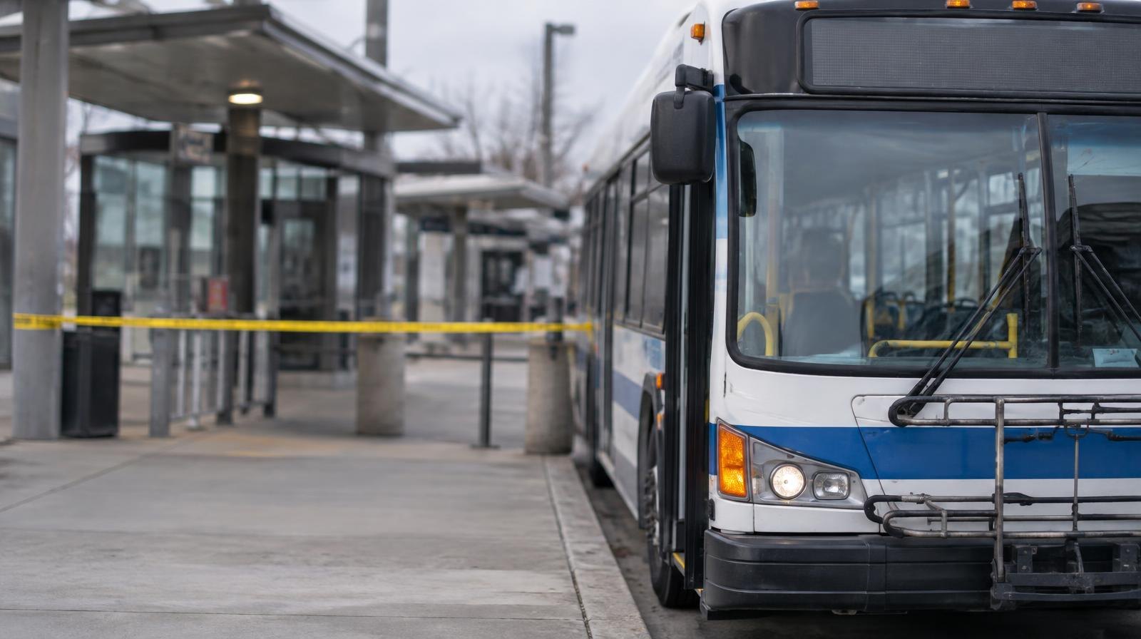 A city bus parked at a deserted transit terminal with yellow caution tape blocking the entrance.