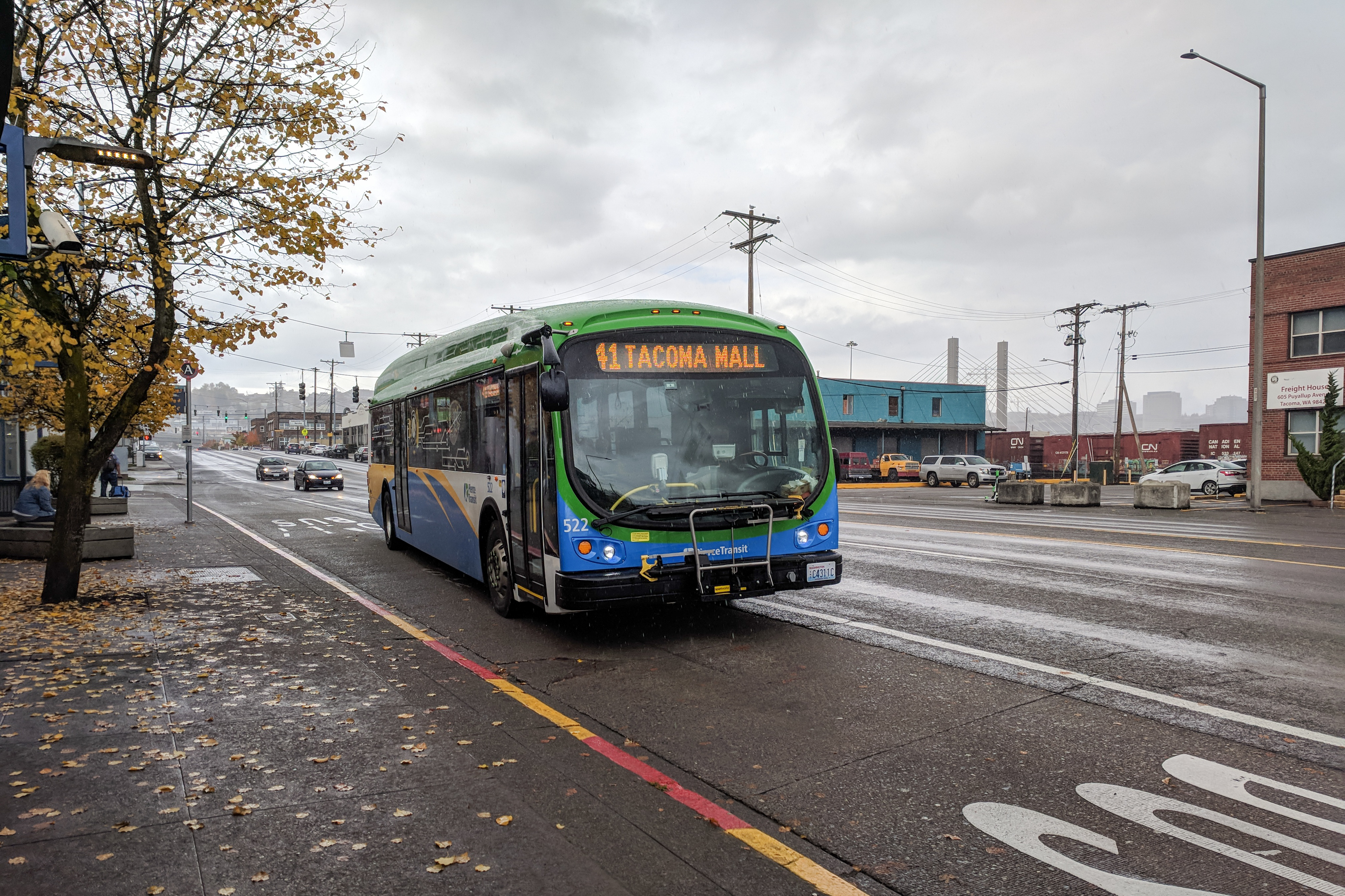 A Pierce Transit bus displaying Route 1 to Tacoma Mall travels on a wet street on an overcast day.