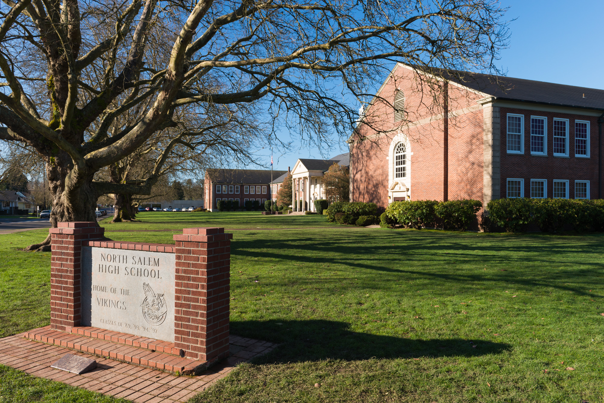 Brick entrance sign for North Salem High School with campus buildings and a bare tree behind it.