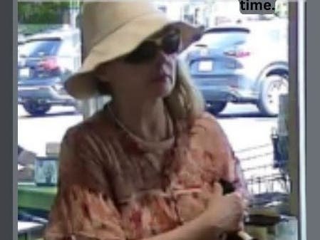 Surveillance still of a woman in a white bucket hat, sunglasses, and pink floral shirt inside a retail store.