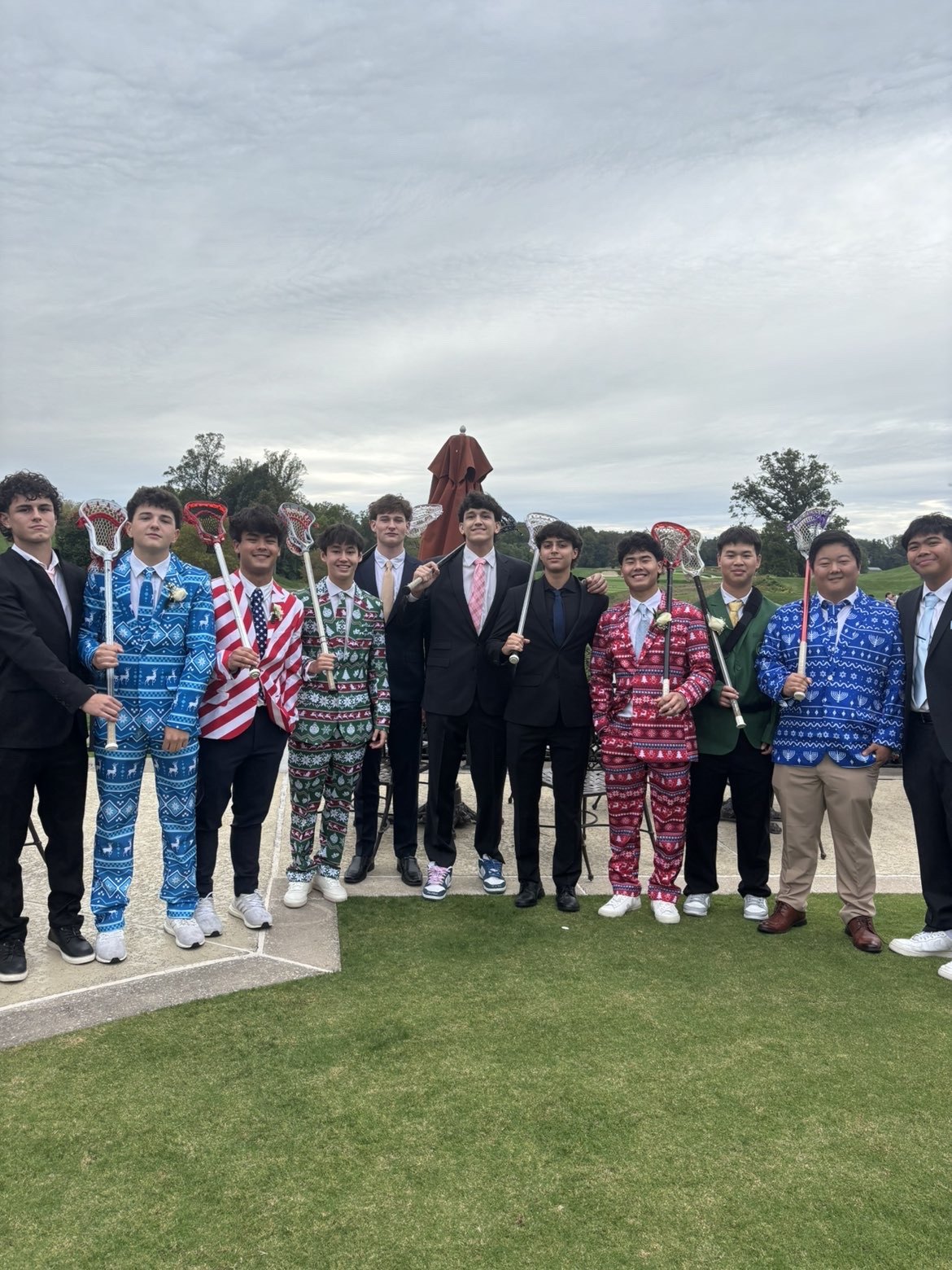 Group of young men in formal suits posing outdoors, several holding lacrosse sticks.