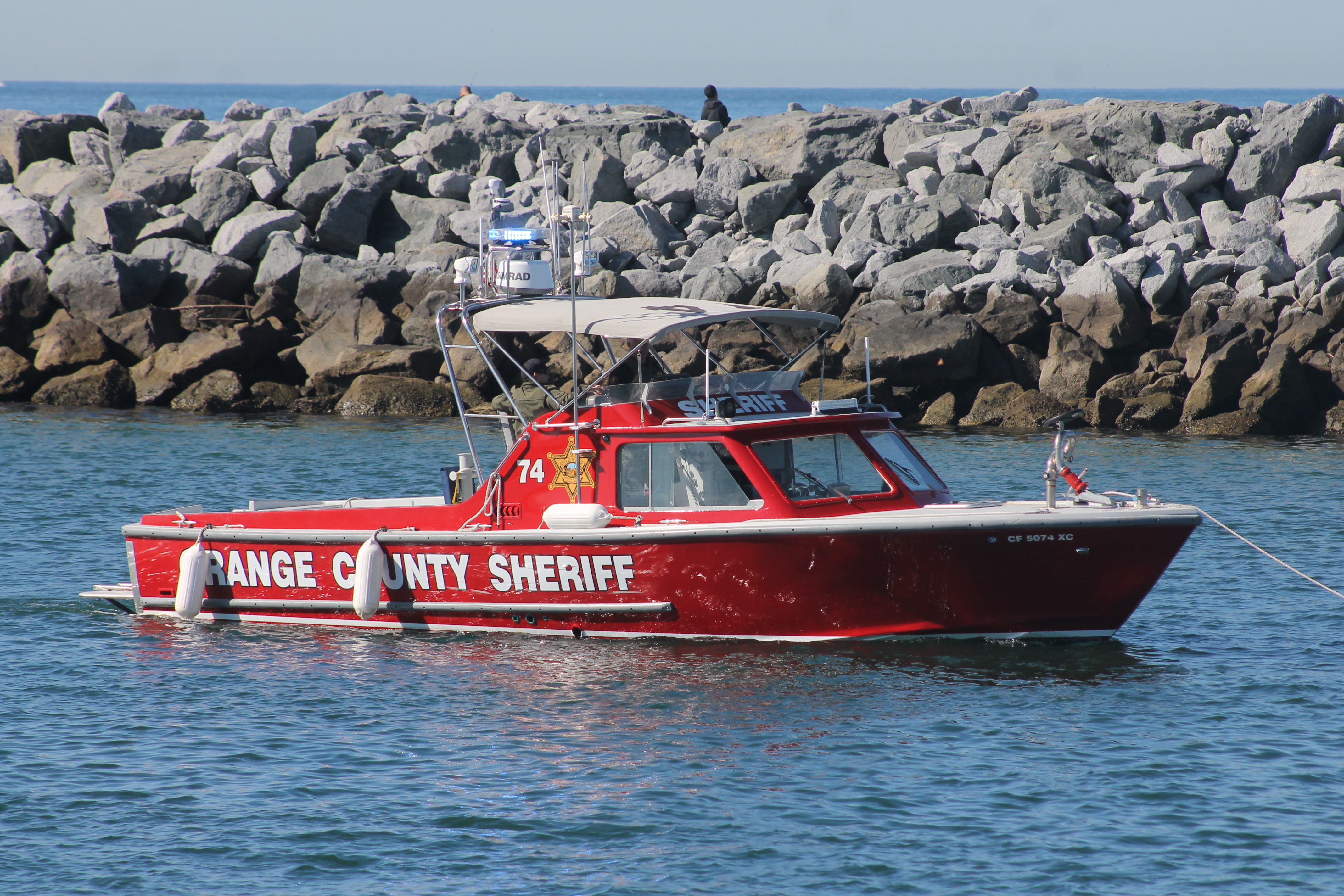 Red sheriff's harbor patrol boat on calm water with seabirds perched on rocks in the background.
