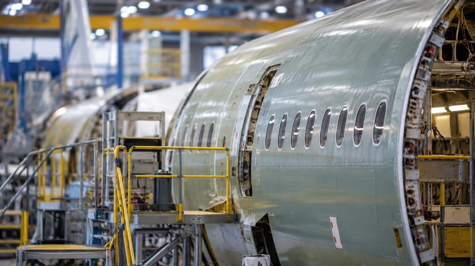 An airplane fuselage surrounded by scaffolding on a factory assembly line.