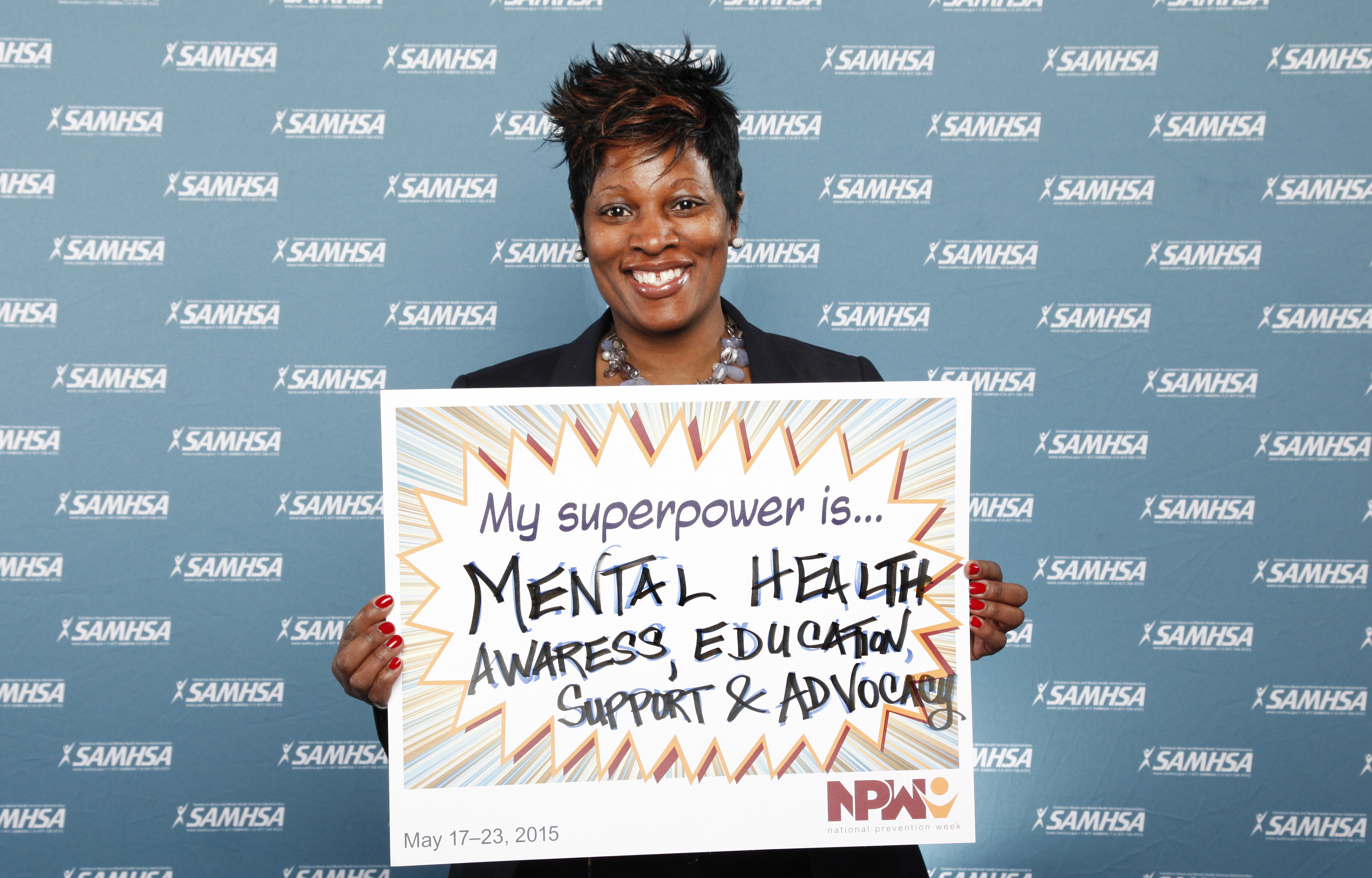Person holding a mental health awareness sign in front of a SAMHSA-branded backdrop.