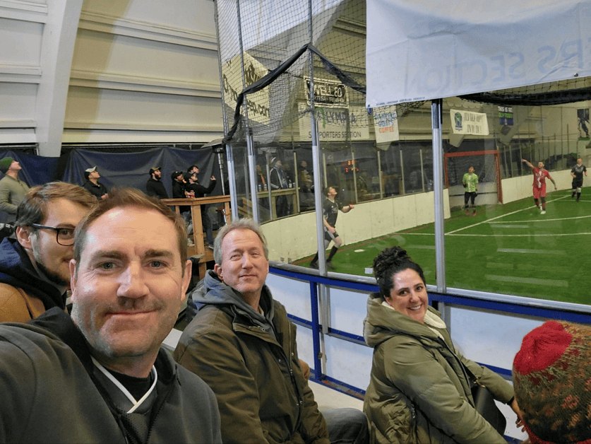 Spectators watching an indoor soccer match through glass boards at an arena.