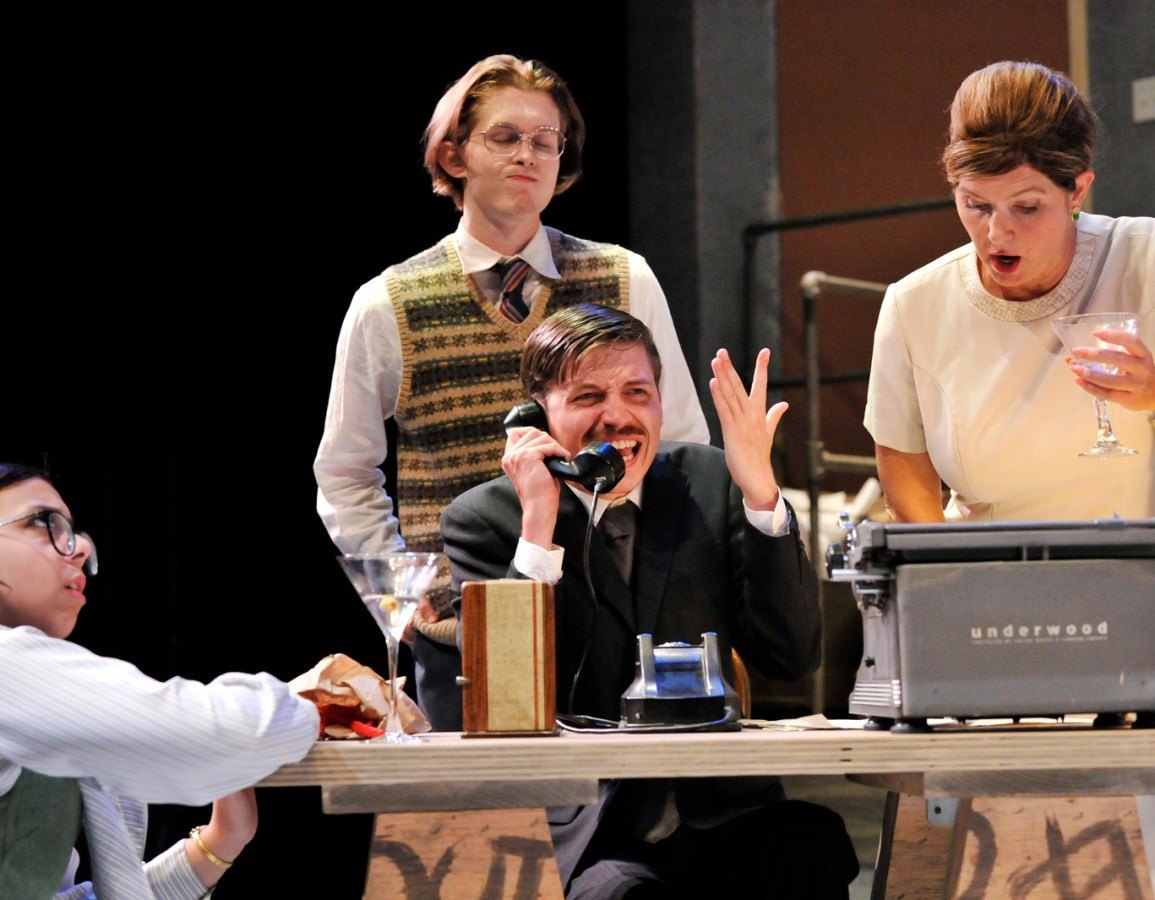 Four actors perform a comedic scene around a desk with a vintage typewriter on stage.