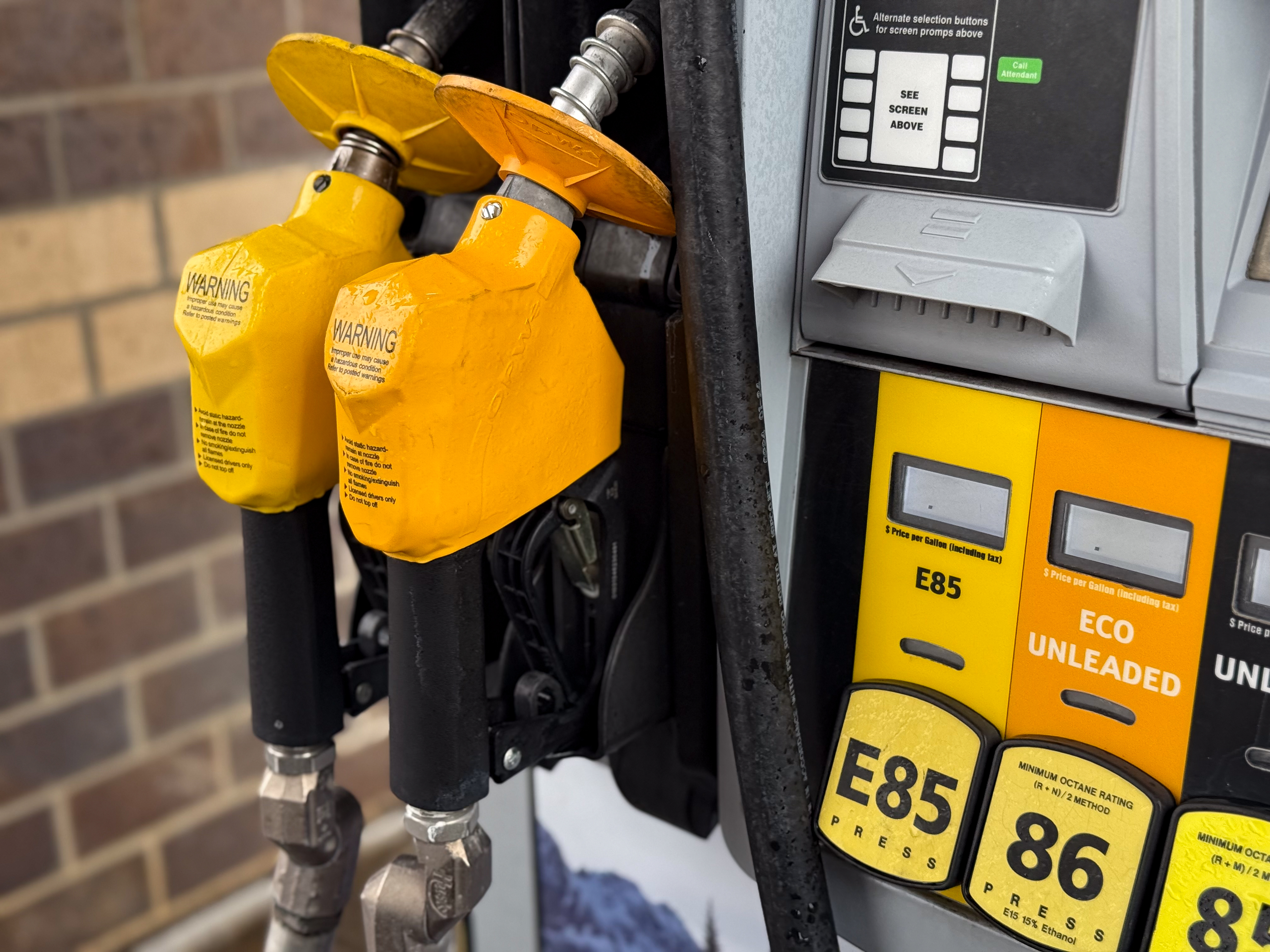 Close-up of a yellow gas pump showing fuel grade options and nozzle holders.