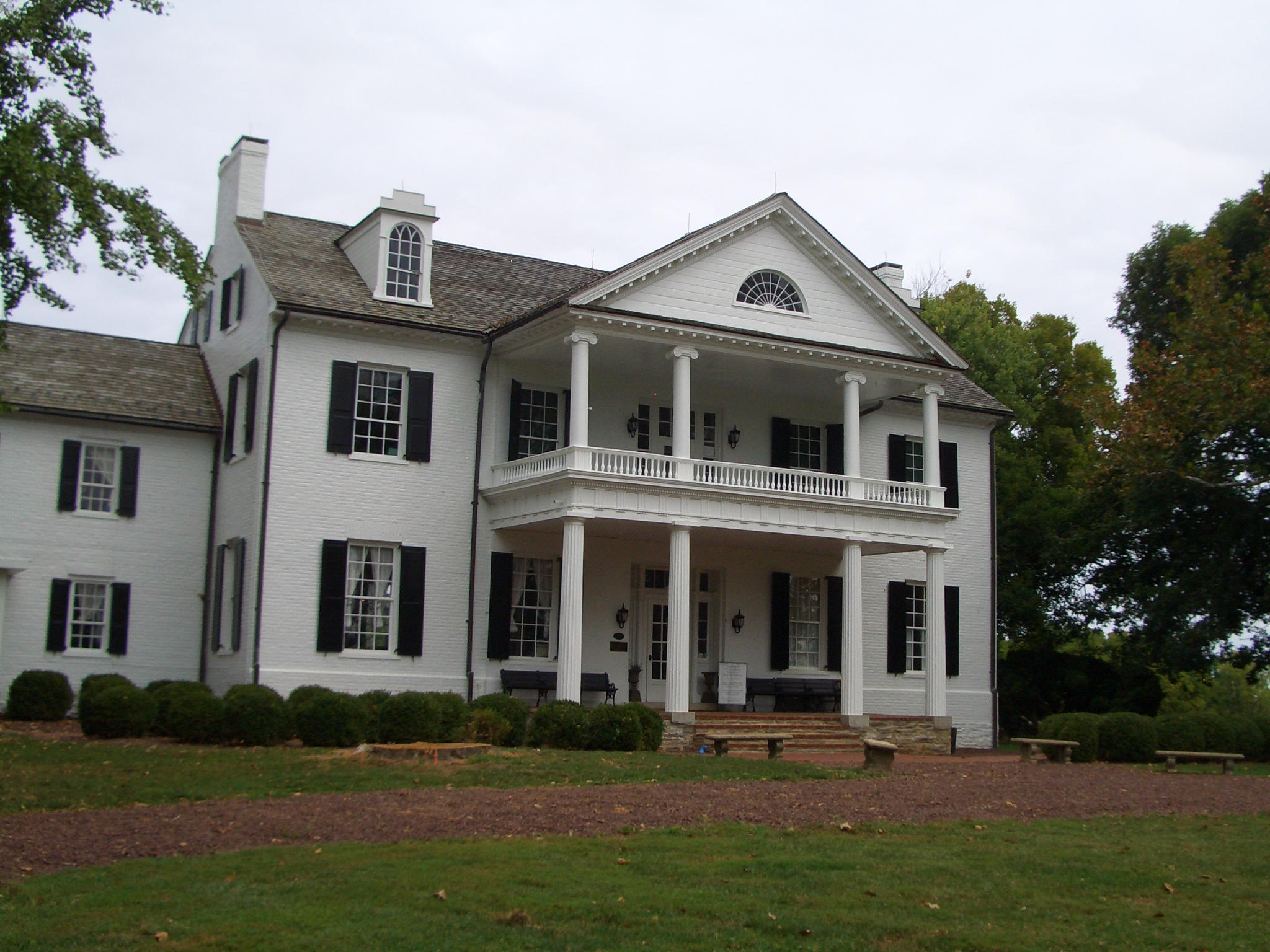 White two-story Greek Revival mansion with tall columns, black shutters, and a triangular pediment.