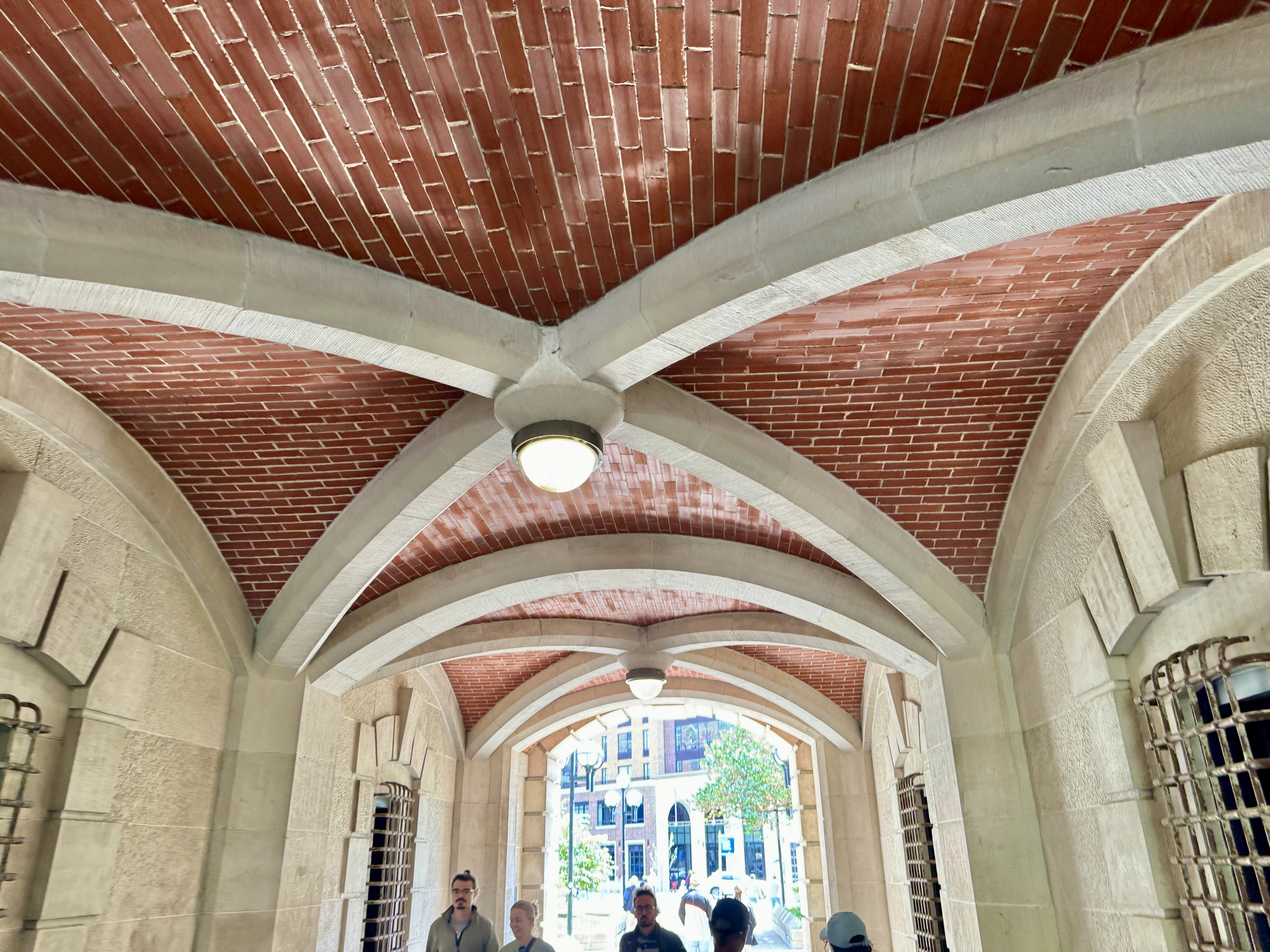 Vaulted brick corridor with white stone arches and hanging lights inside a historic university building.