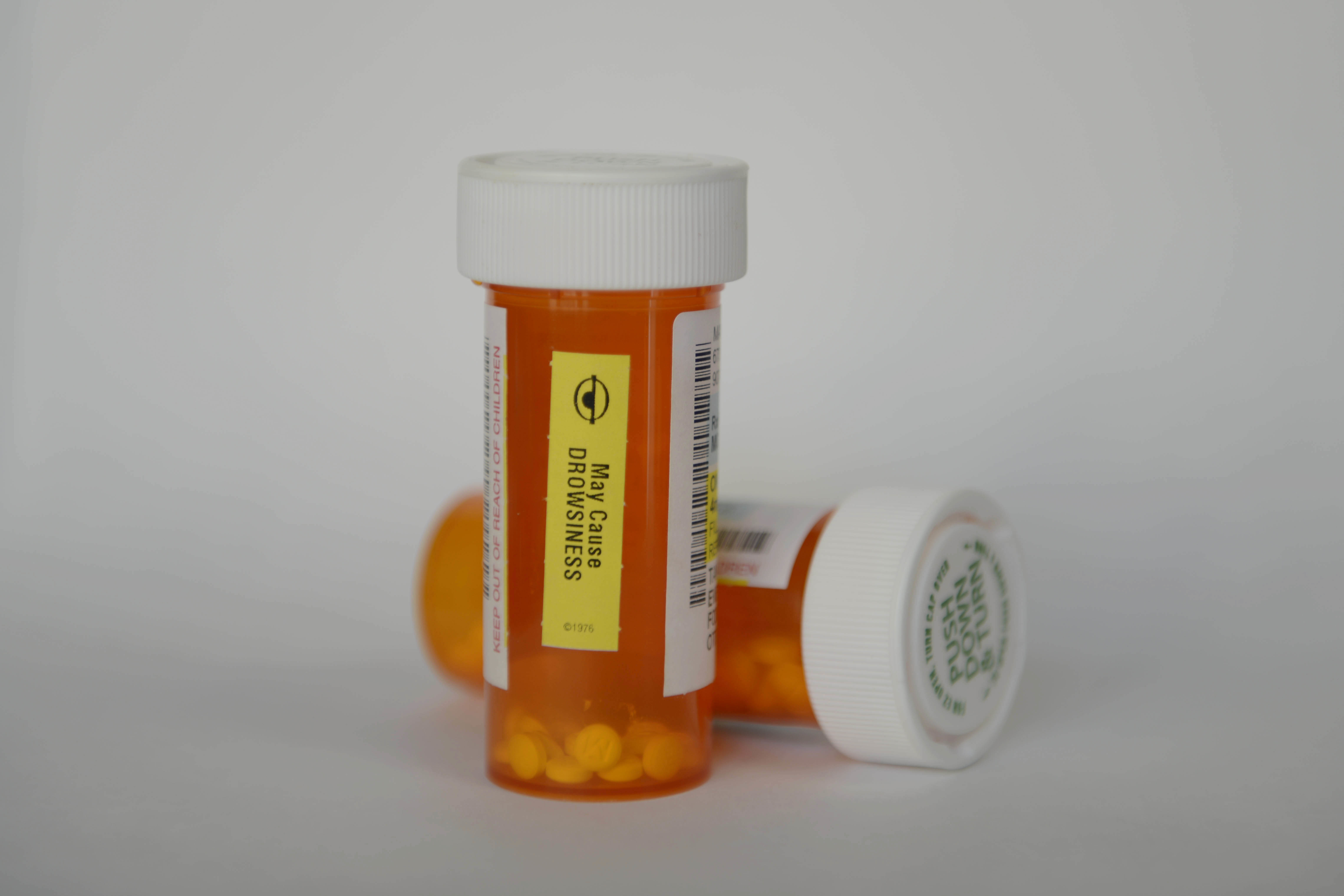Two orange prescription medication bottles with white caps on a gray background.