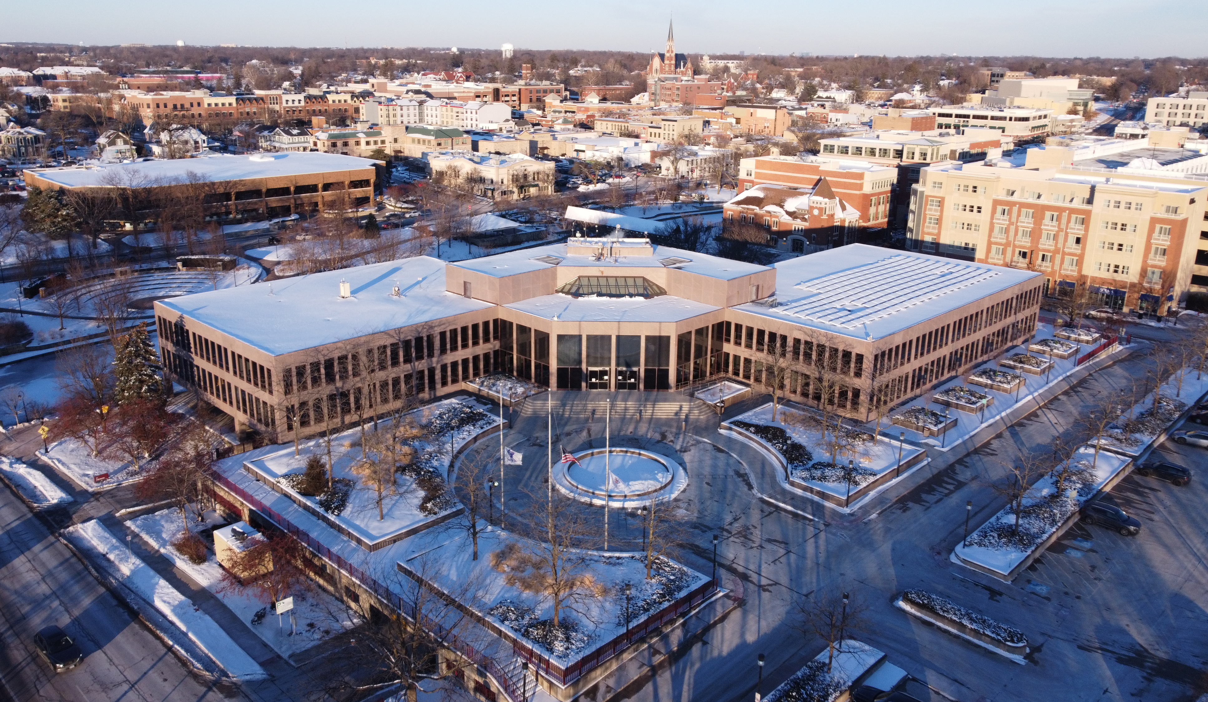 Aerial winter view of a large civic building with snow-covered grounds and multiple flagpoles.