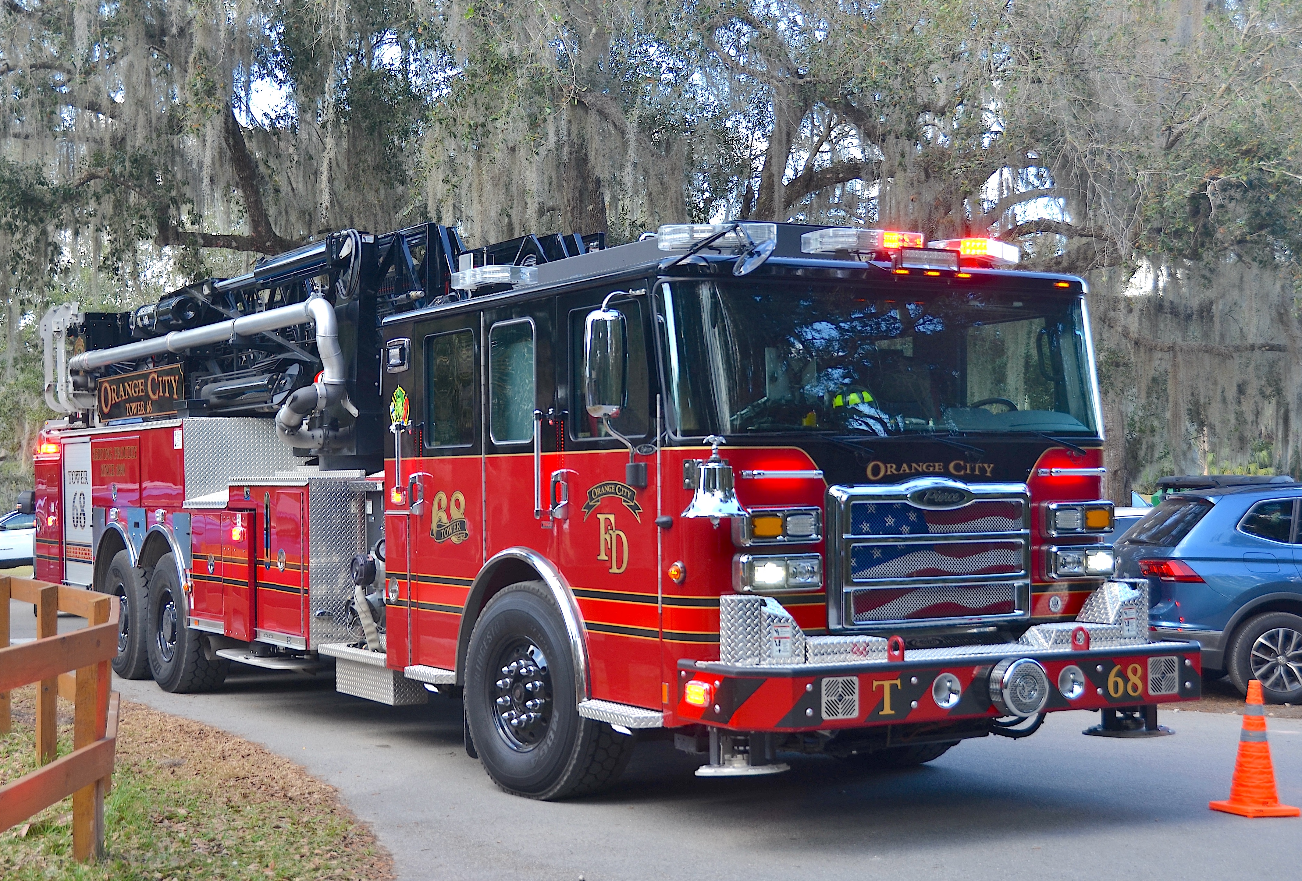 Red aerial ladder fire truck with emergency lights on, parked outdoors.