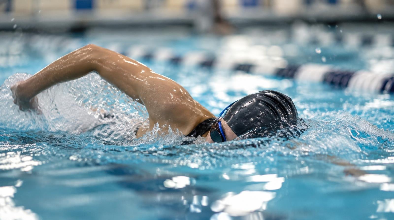 A swimmer mid-stroke in a pool lane wearing goggles and a swim cap.