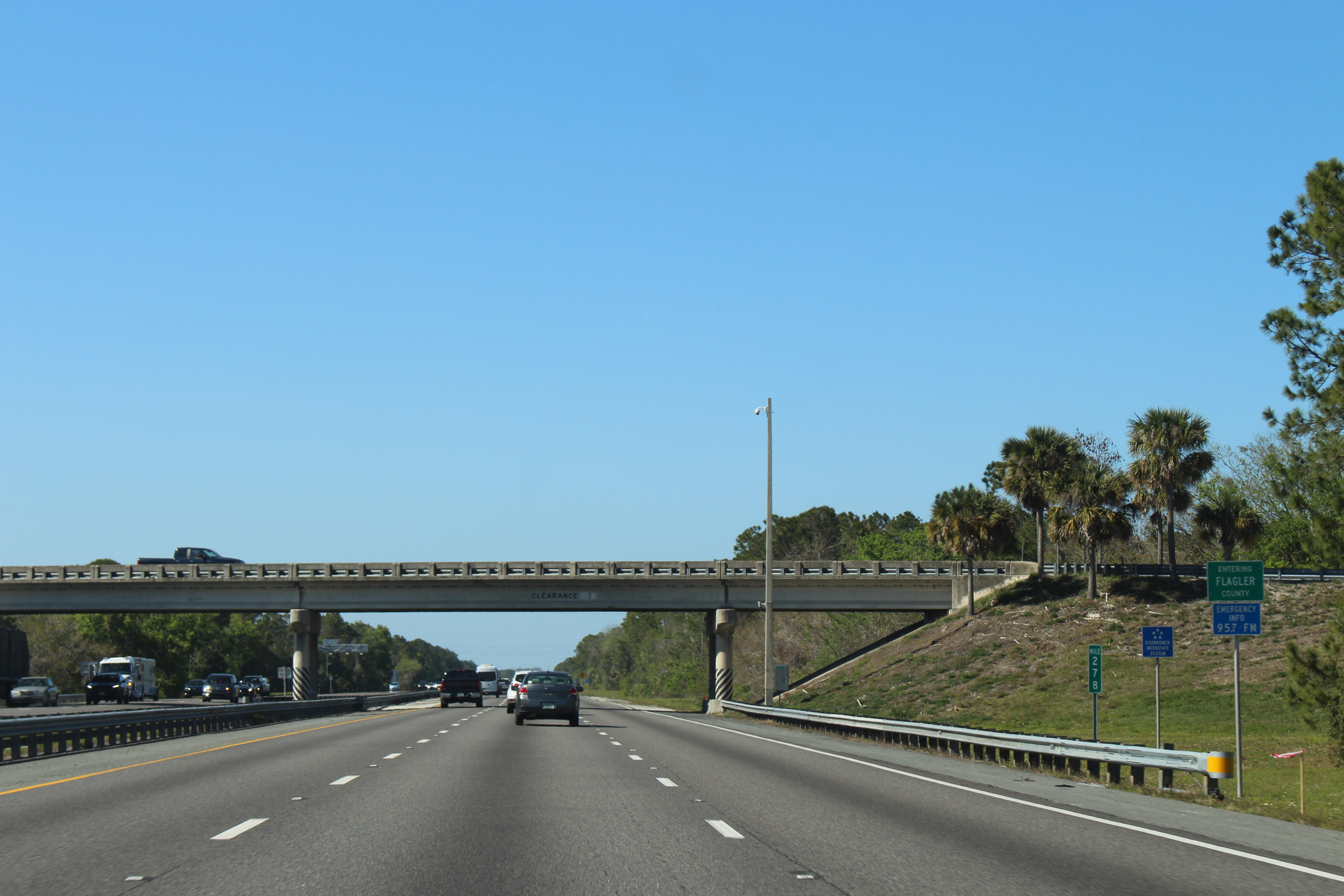 Multi-lane northbound Interstate 95 in Florida with an overpass and palm trees.