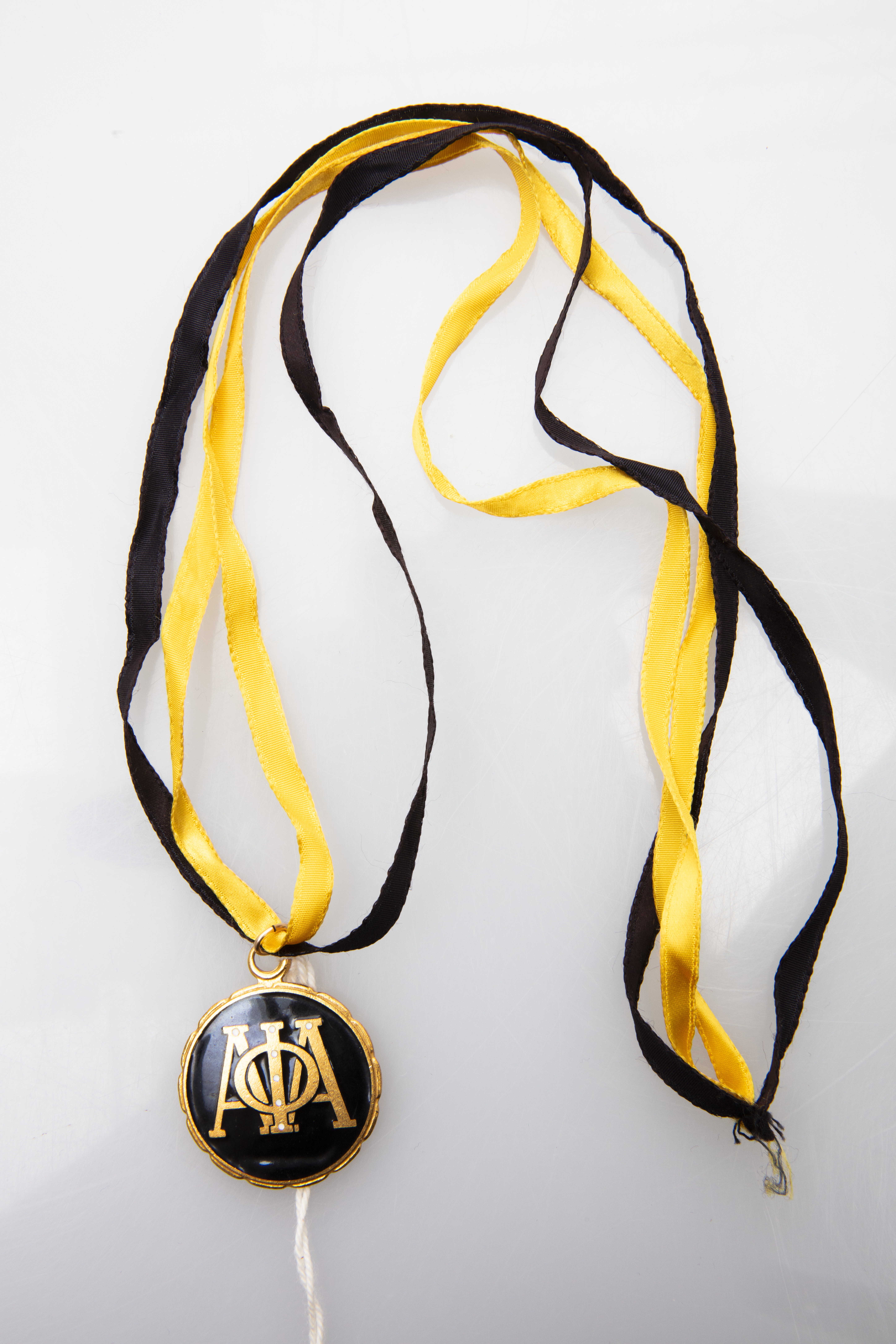 Black and gold Alpha Phi Alpha fraternity medallion on a two-toned ribbon.