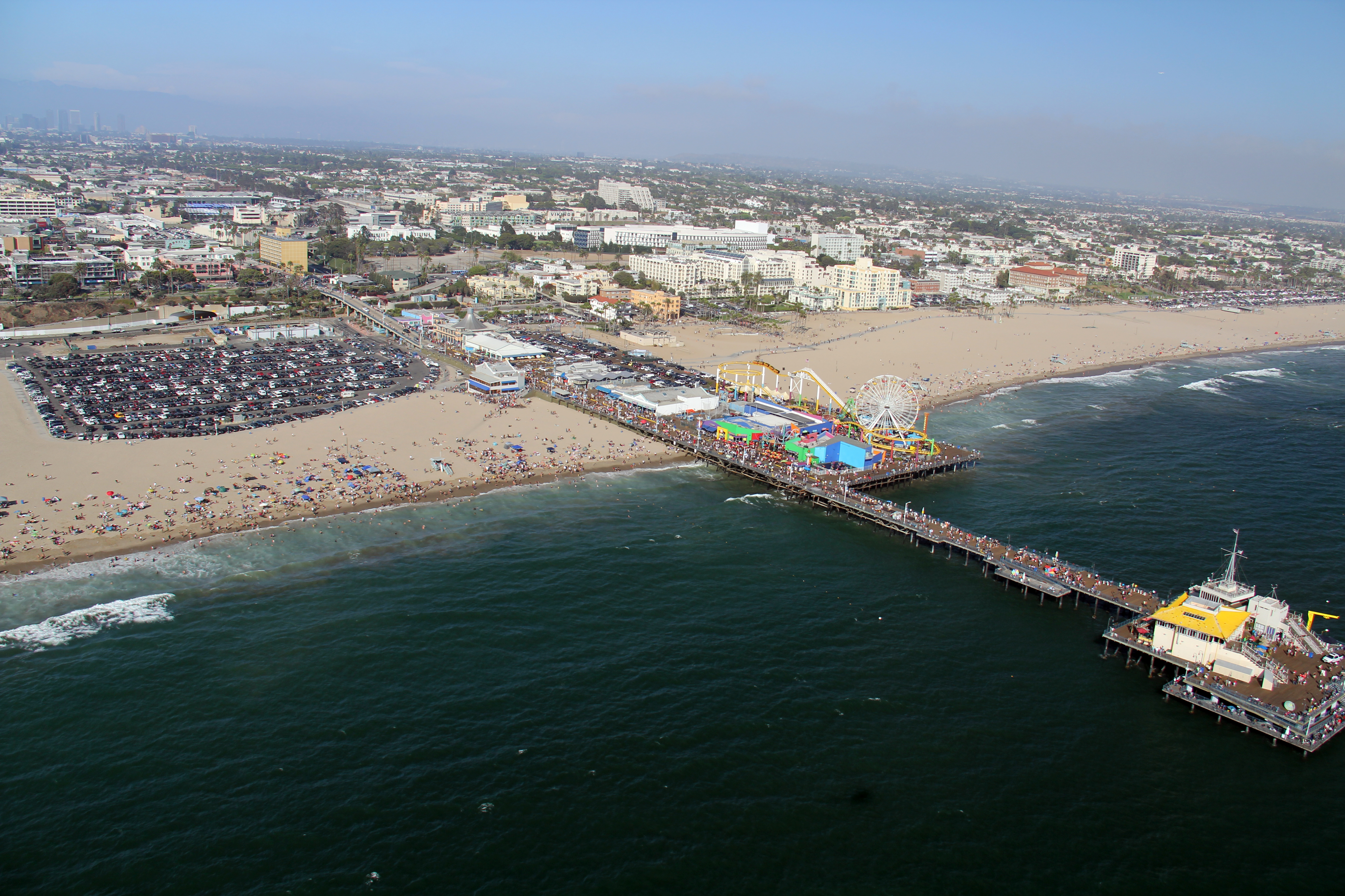 Aerial view of Santa Monica Pier with Ferris wheel and beachgoers below.