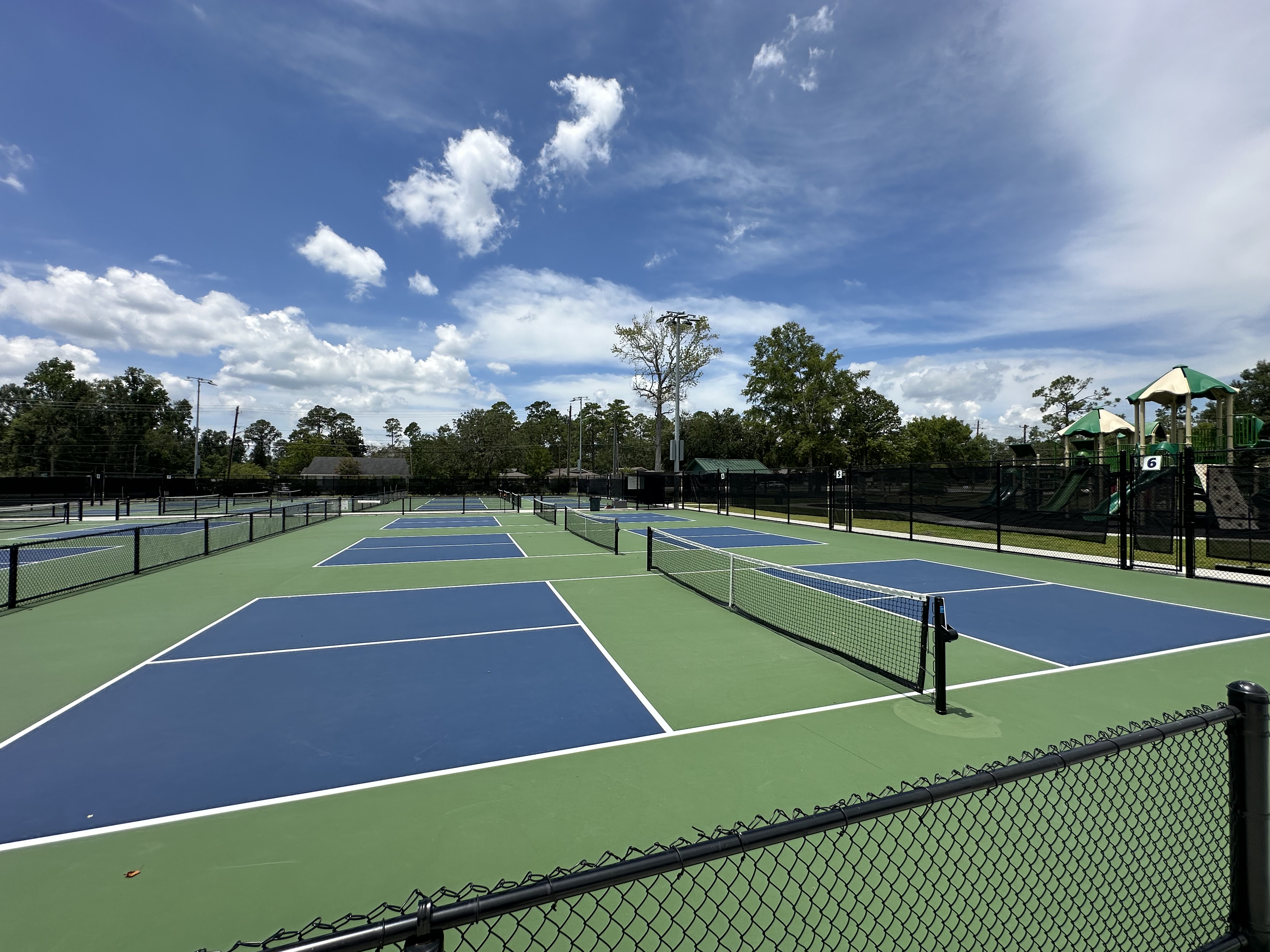 Three outdoor pickleball courts with blue and green surfaces, nets, and fencing.