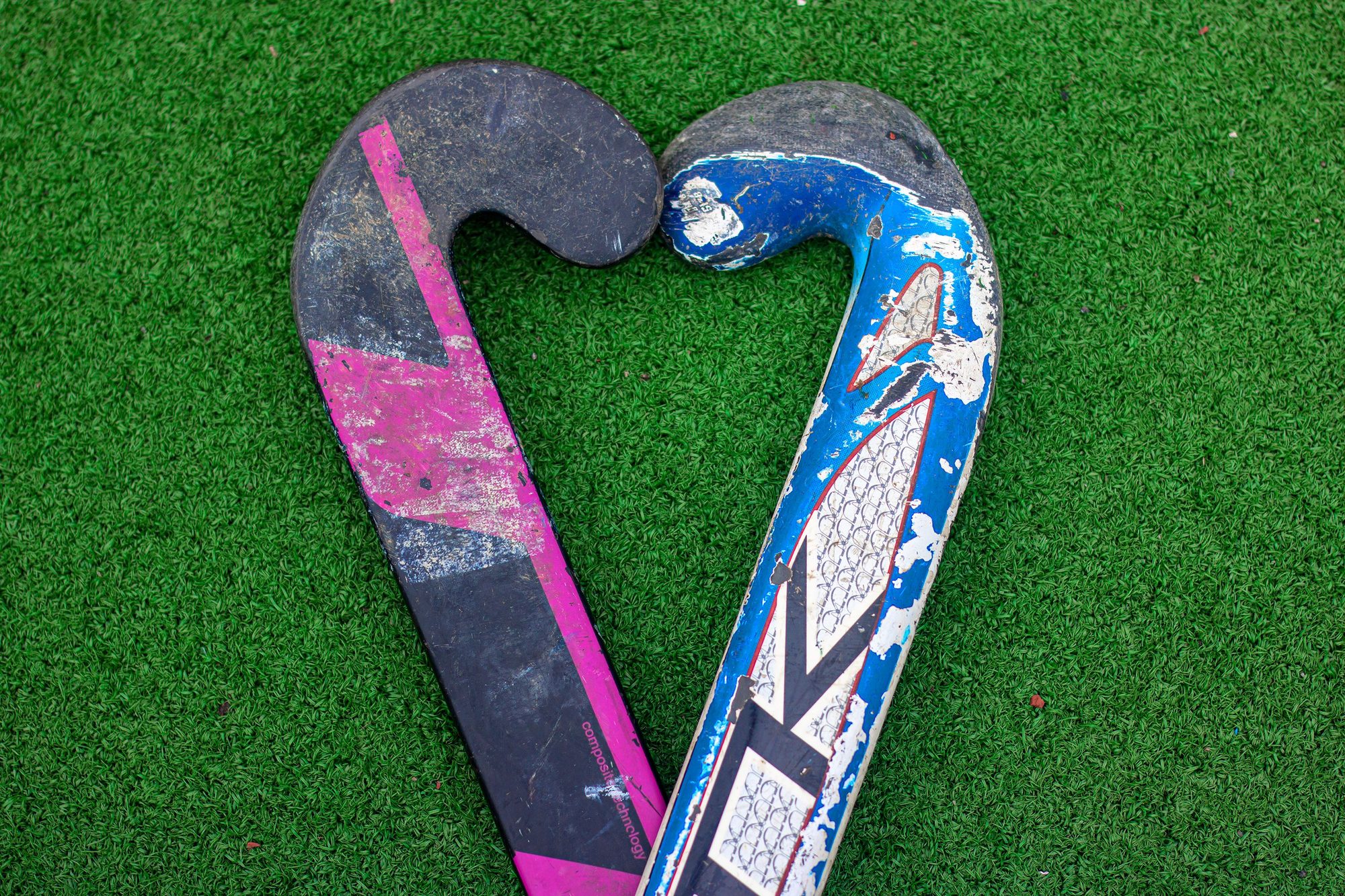 Two field hockey sticks forming a heart shape on green turf.