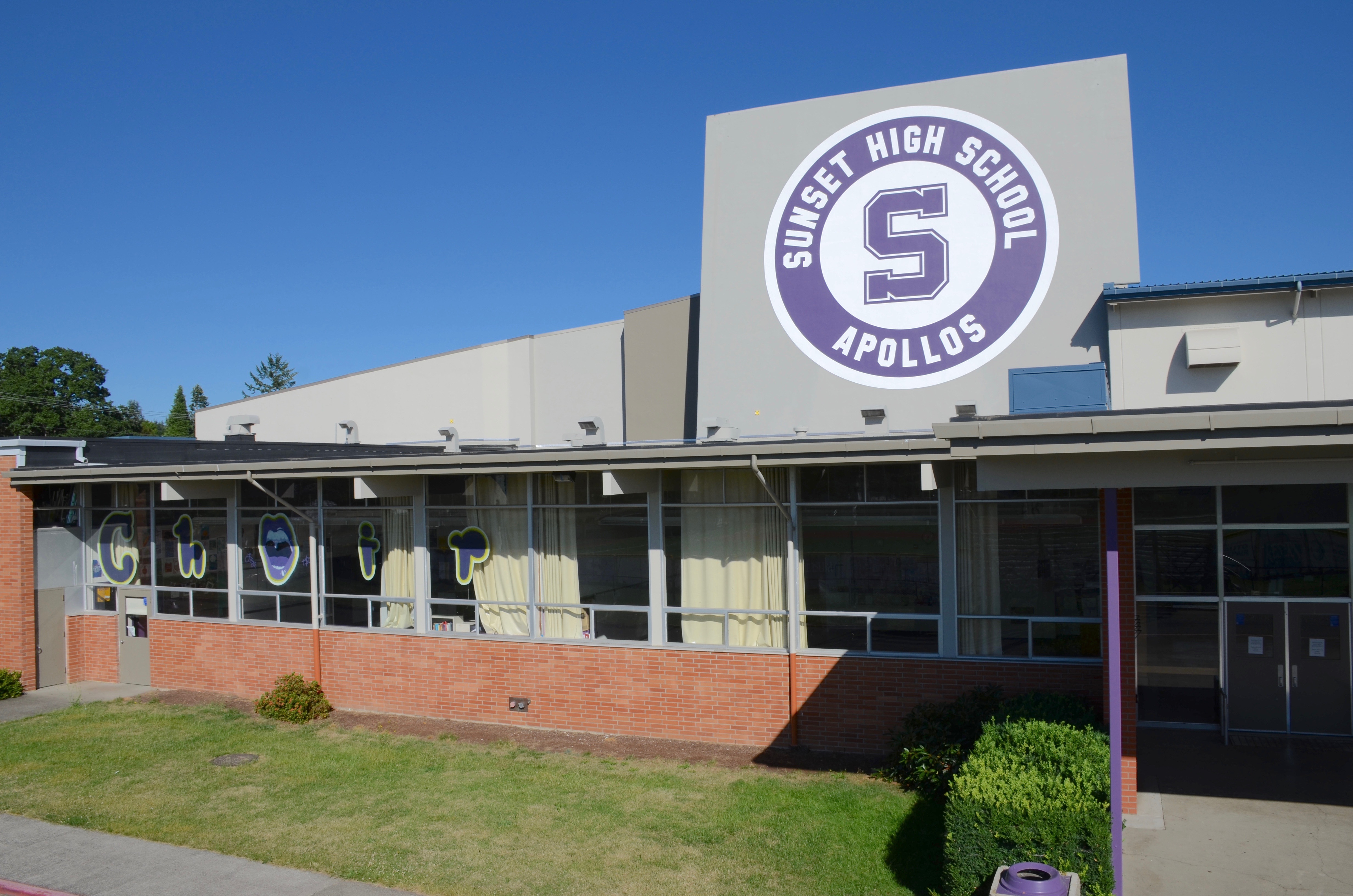 Exterior of a high school building with a large purple circular school logo on the brick facade.