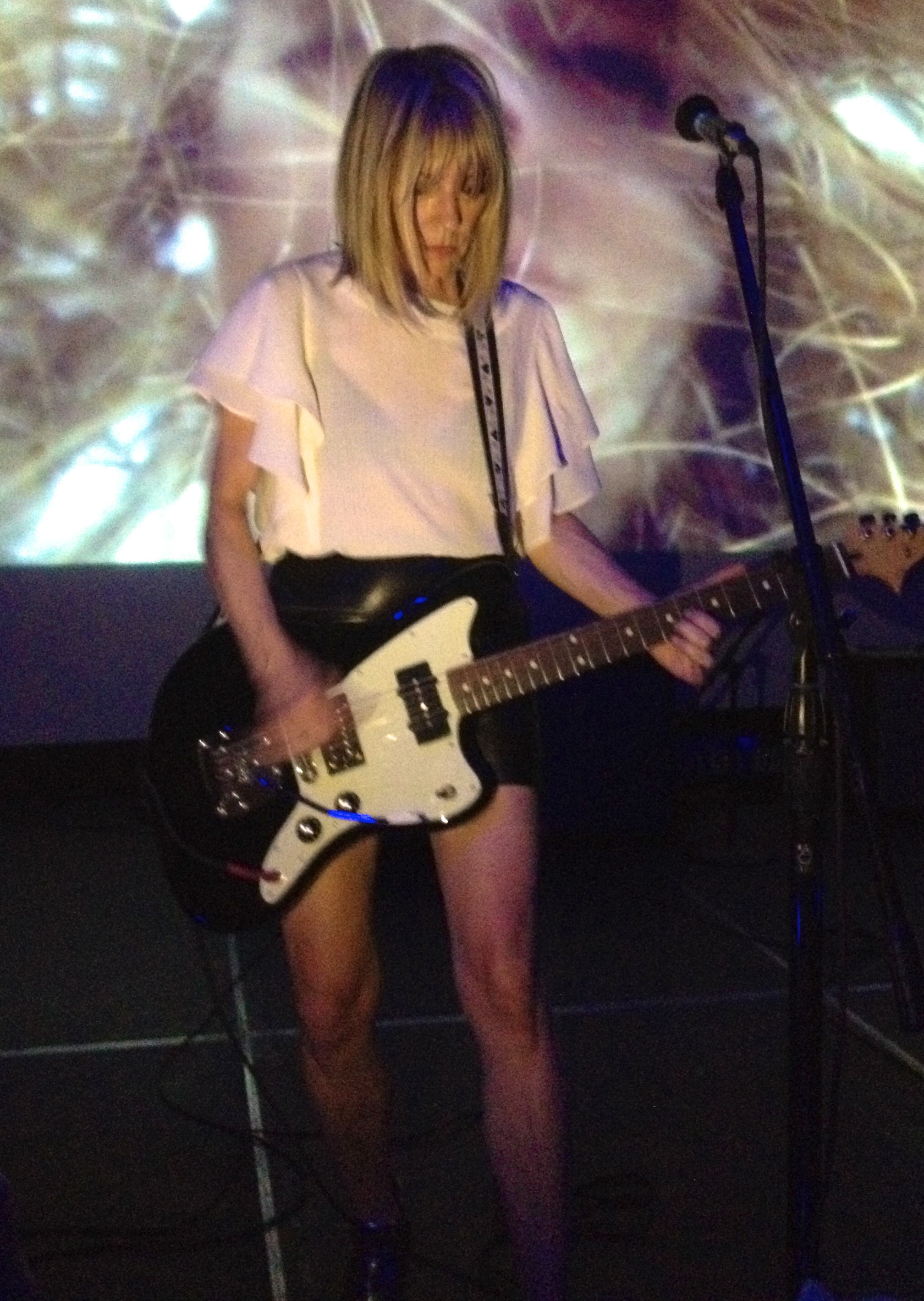 A guitarist performs on a dimly lit stage with a large projected image behind them.