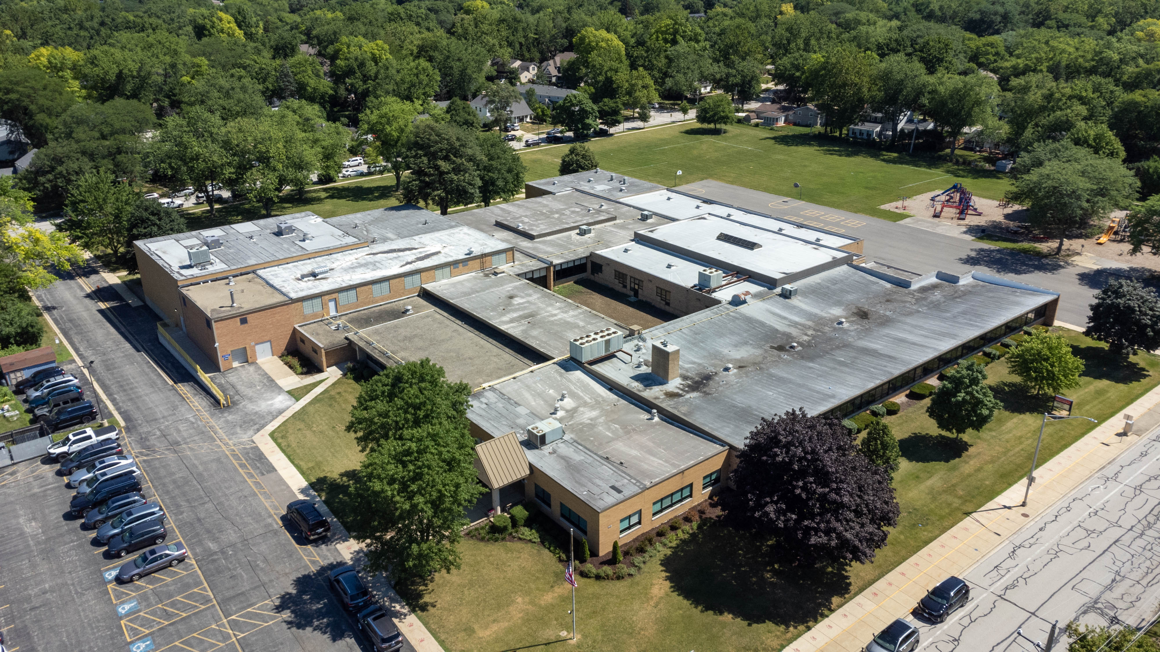 Aerial view of a multi-wing flat-roofed elementary school campus with a parking lot and playground.