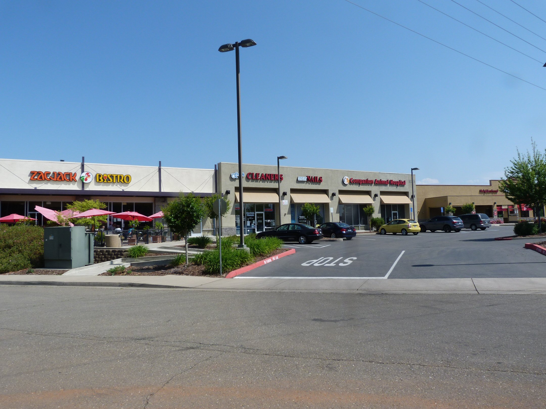 Strip mall with several storefronts and a parking lot on a sunny day