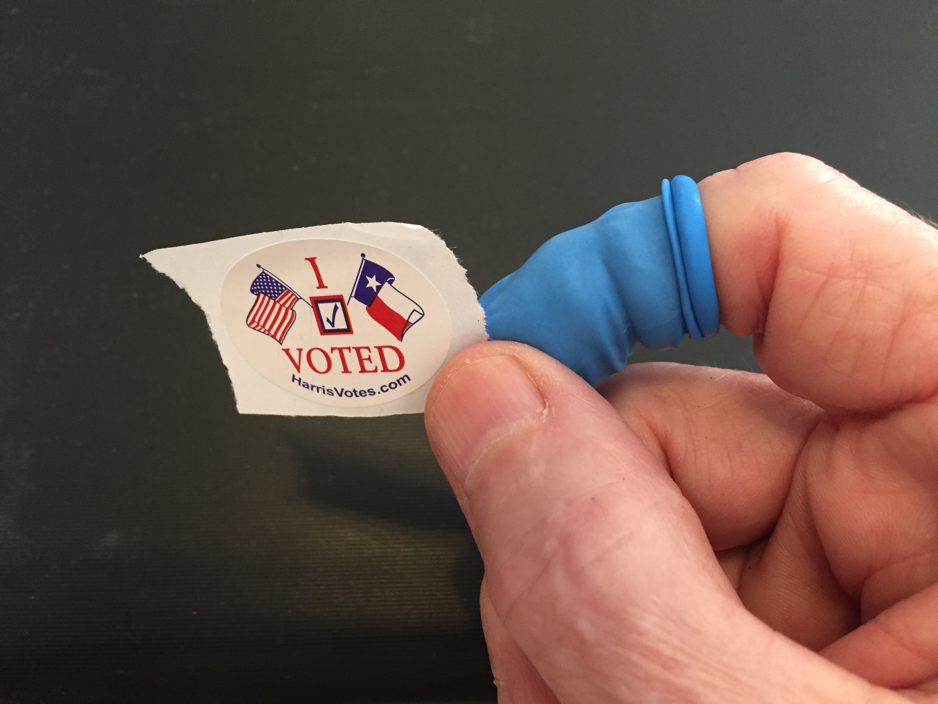 A hand holds an 'I Voted' sticker from Harris County, Texas.