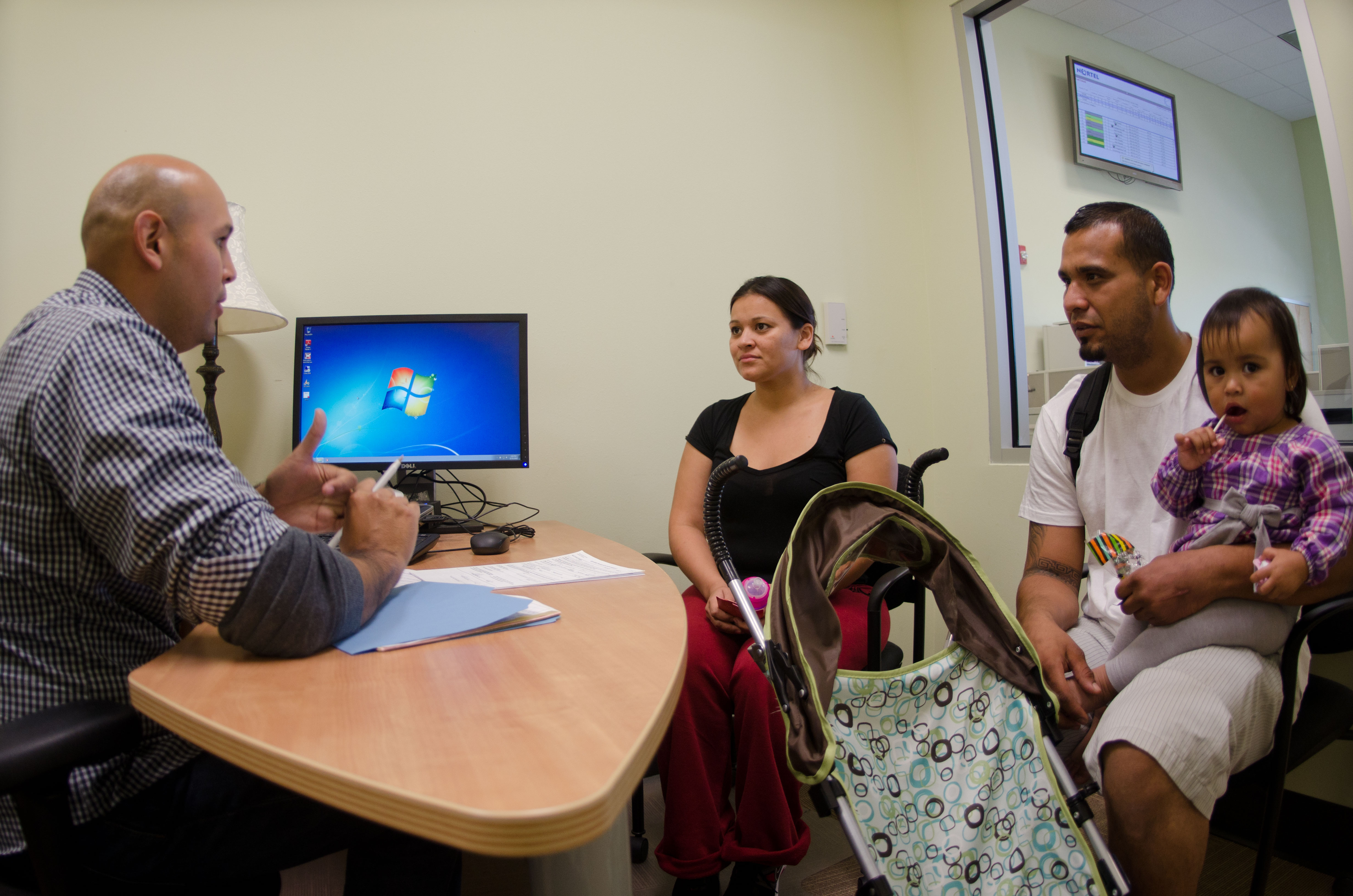 A family of three seated across a desk from an outreach specialist in an office setting.