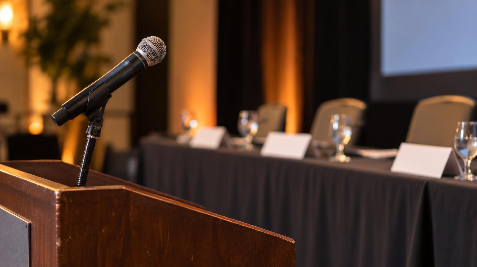 A microphone on a podium faces a long judges' table with nameplates and water glasses.