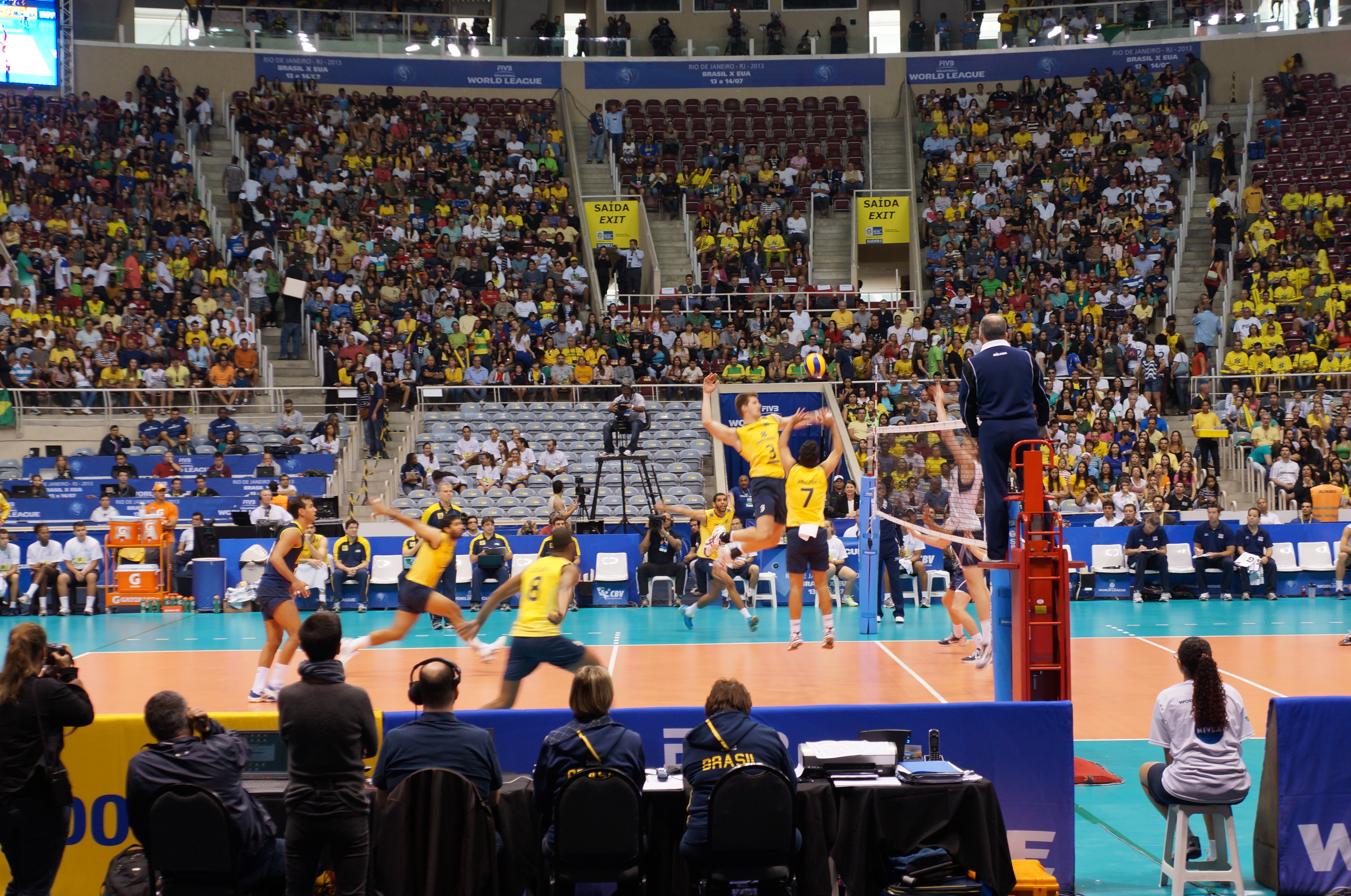 A volleyball player jumps to spike the ball at the net during an indoor match.