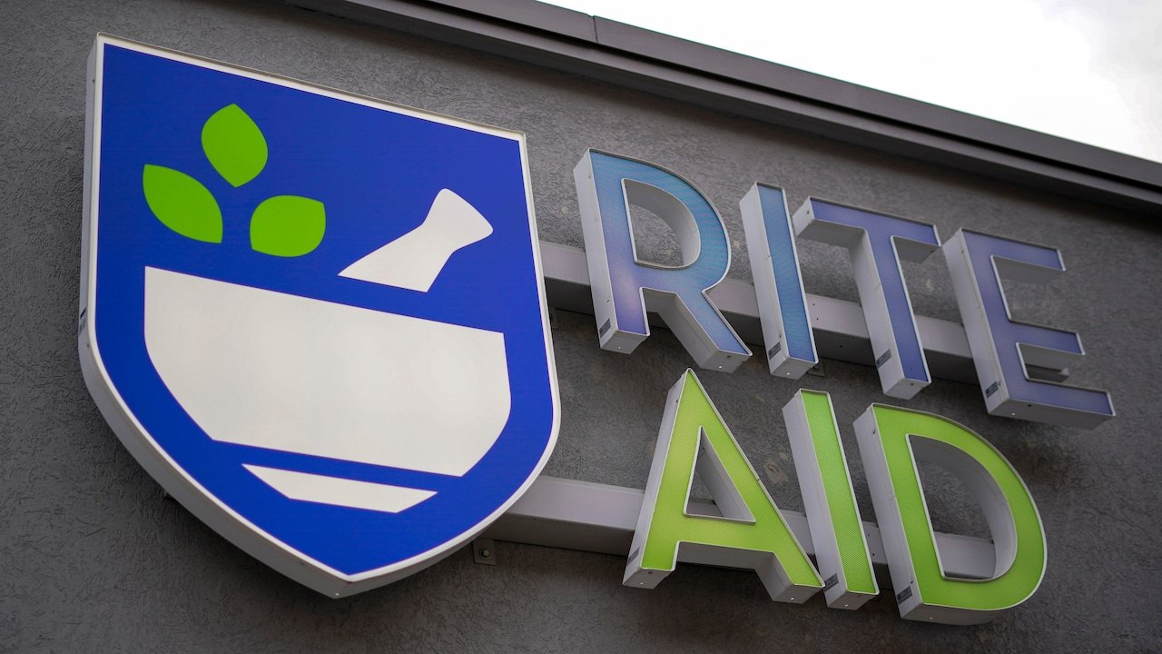 Rite Aid exterior sign with blue shield logo and green lettering on a building facade.