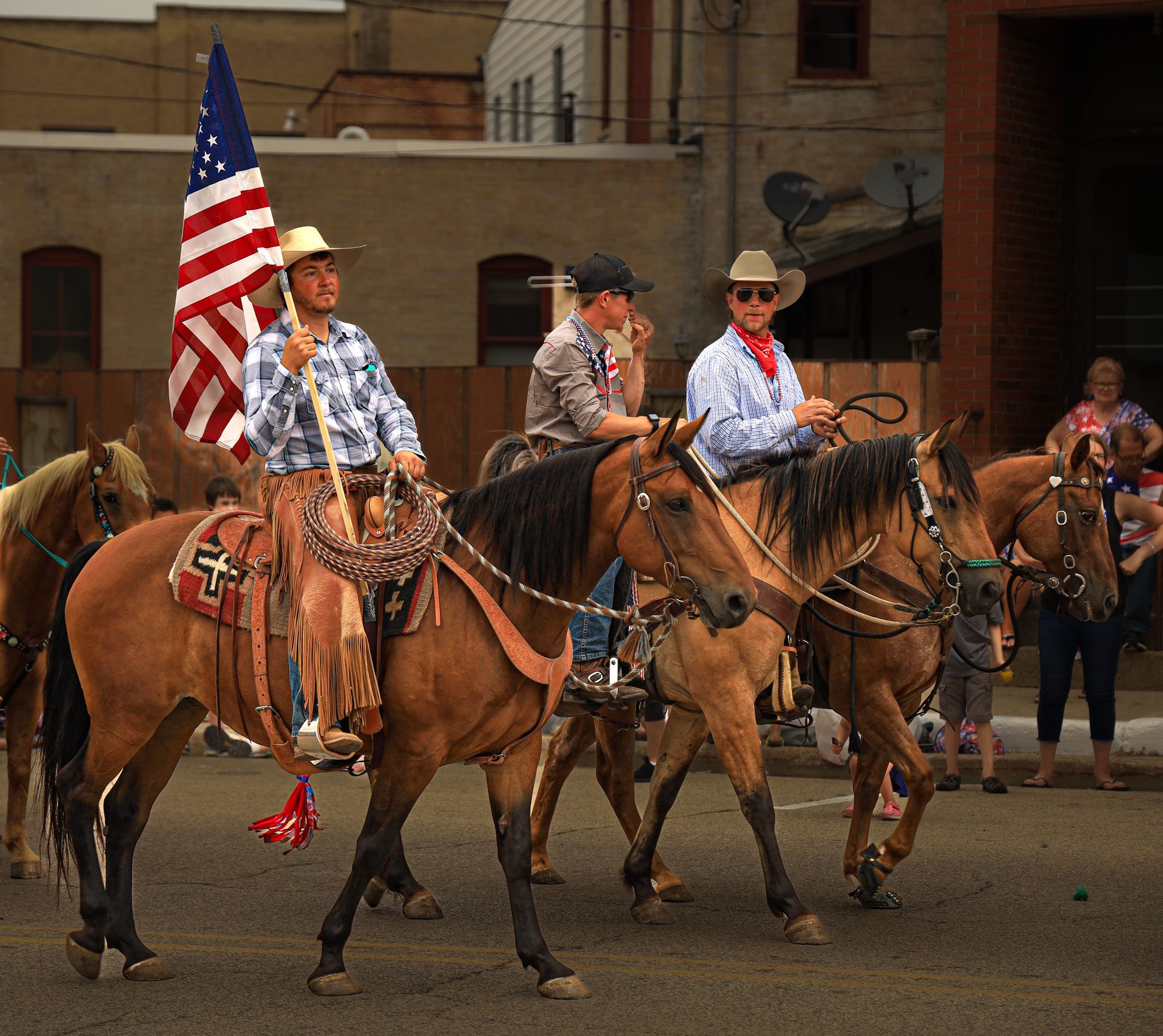 Cowboys parade with horses and American flag on a sunny day outdoors.