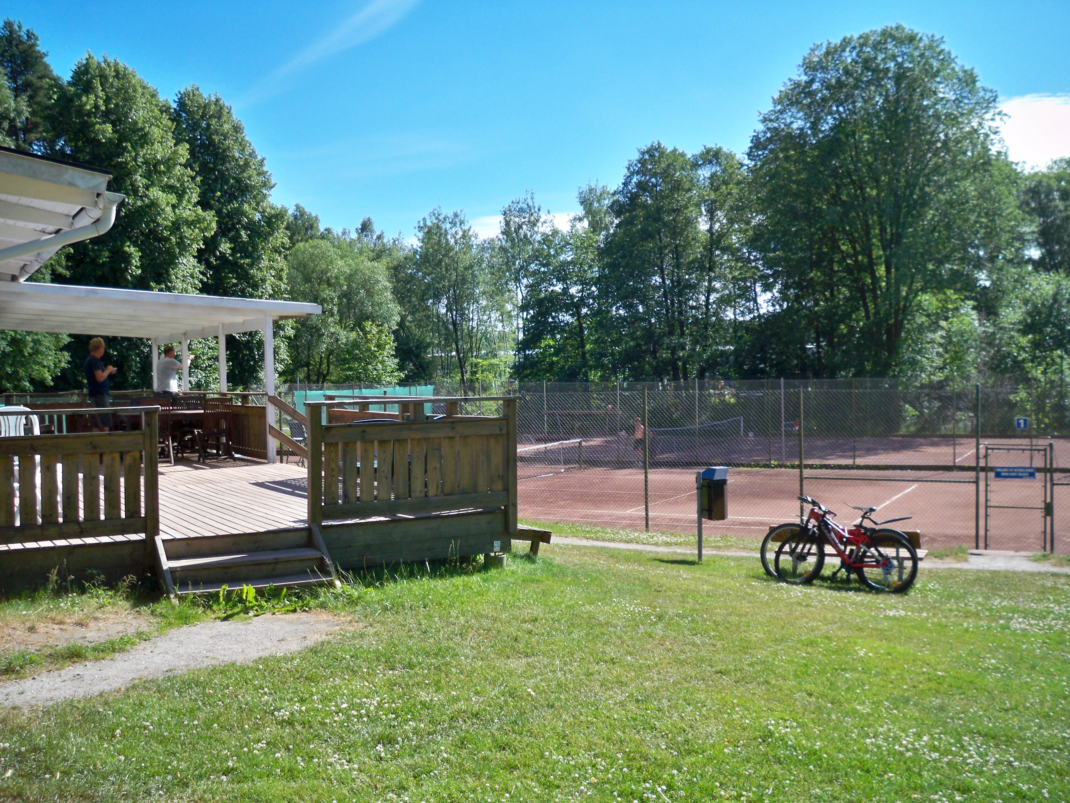 Two outdoor clay tennis courts behind chain-link fencing on a sunny day.