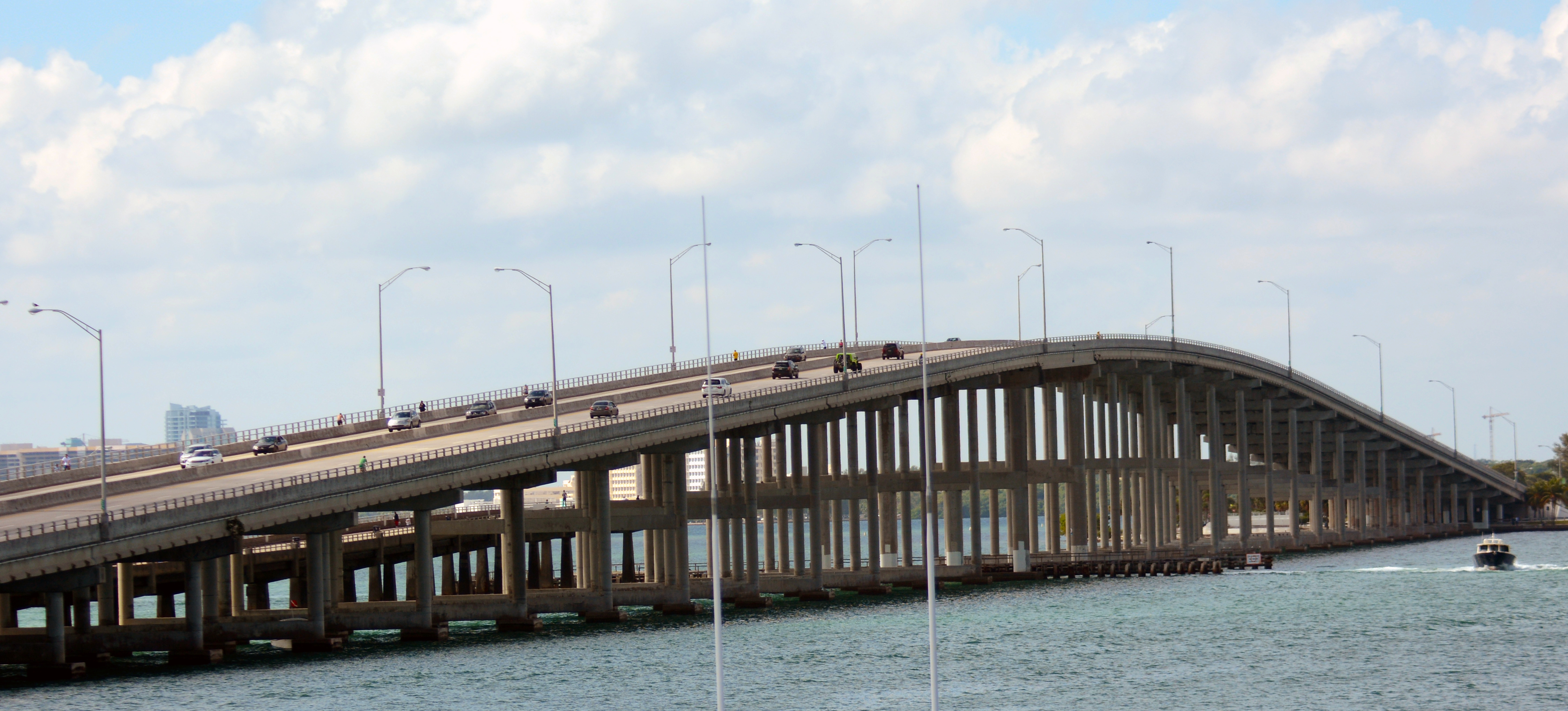 Elevated multi-lane bridge over blue water with light poles and vehicles traveling across it.
