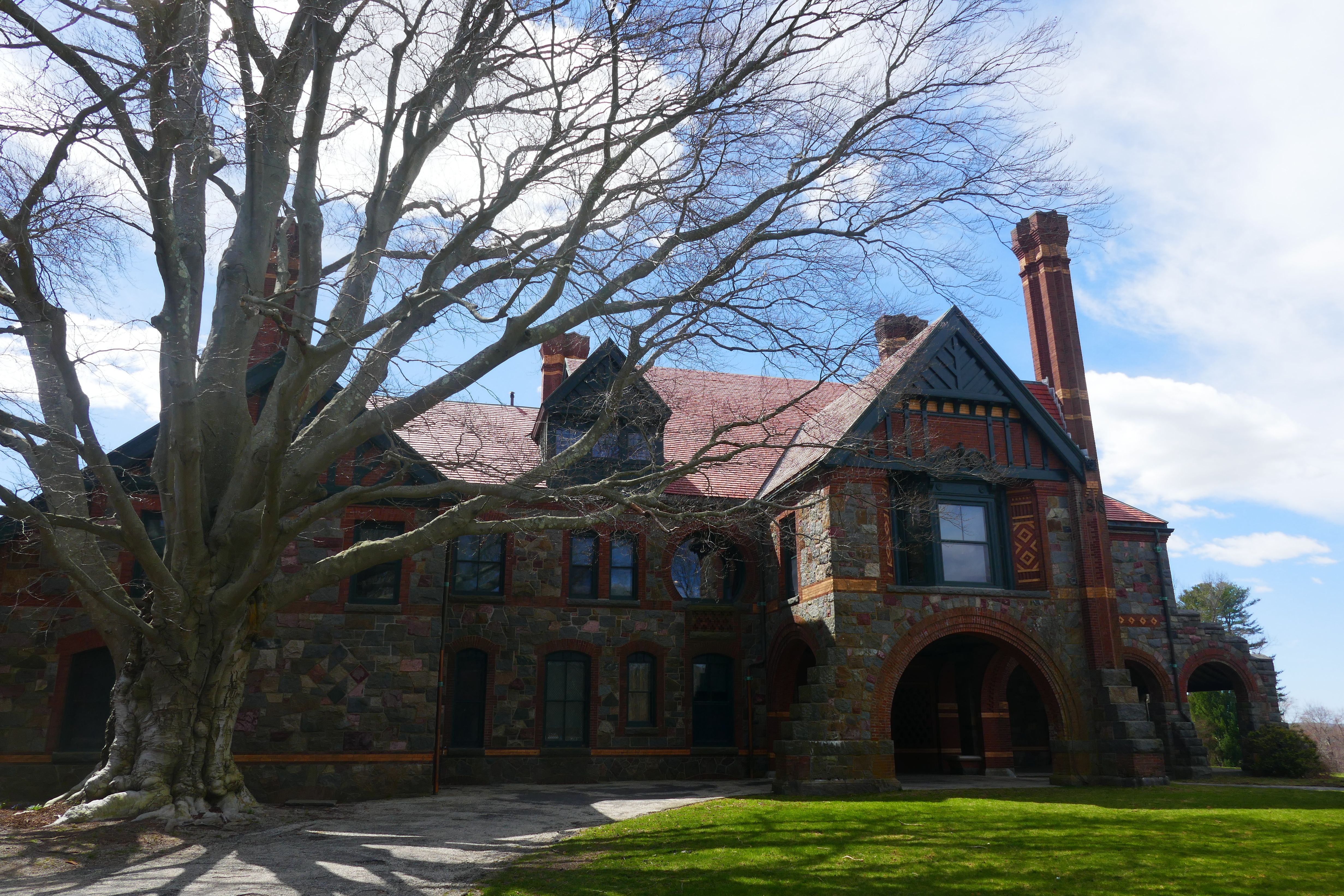 Victorian stone mansion with multiple chimneys and arched entryway on a green lawn