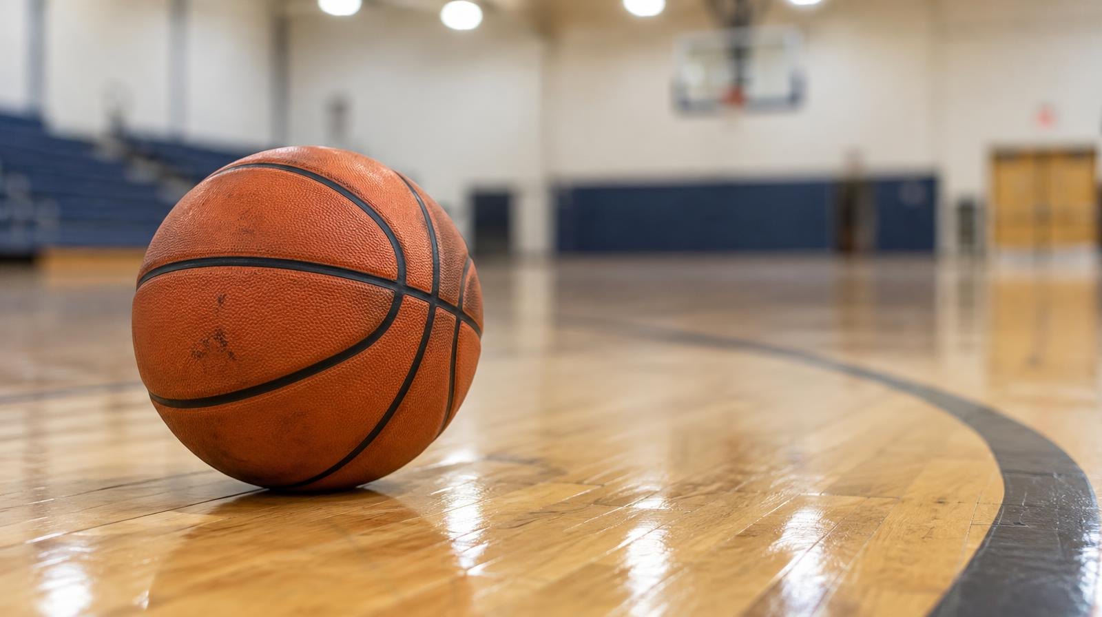An orange basketball resting on a hardwood gym floor beside a painted arc line.