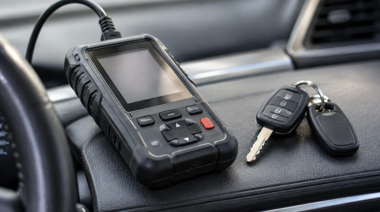A small handheld electronic key programmer device and car keys on a dashboard.