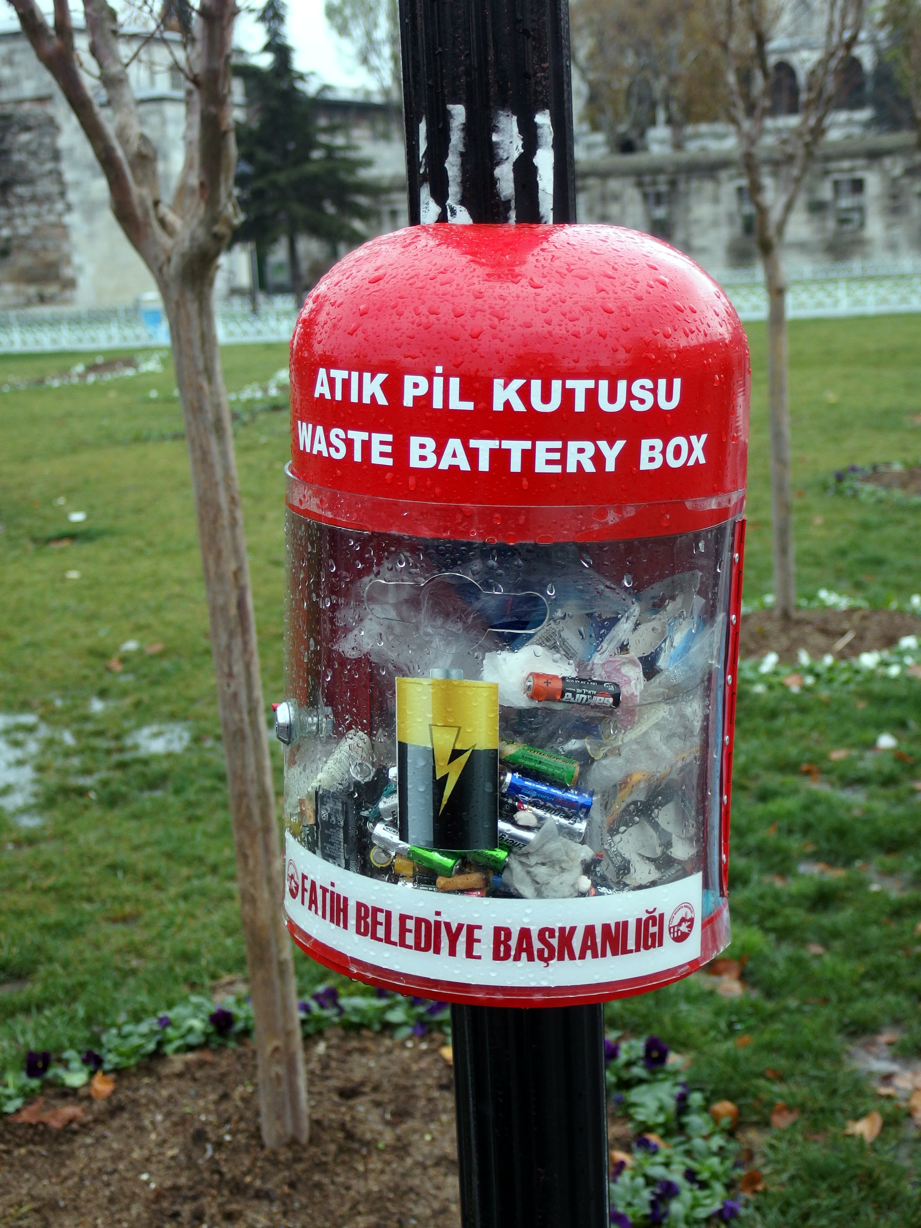 Red transparent collection box on a pole filled with used batteries.