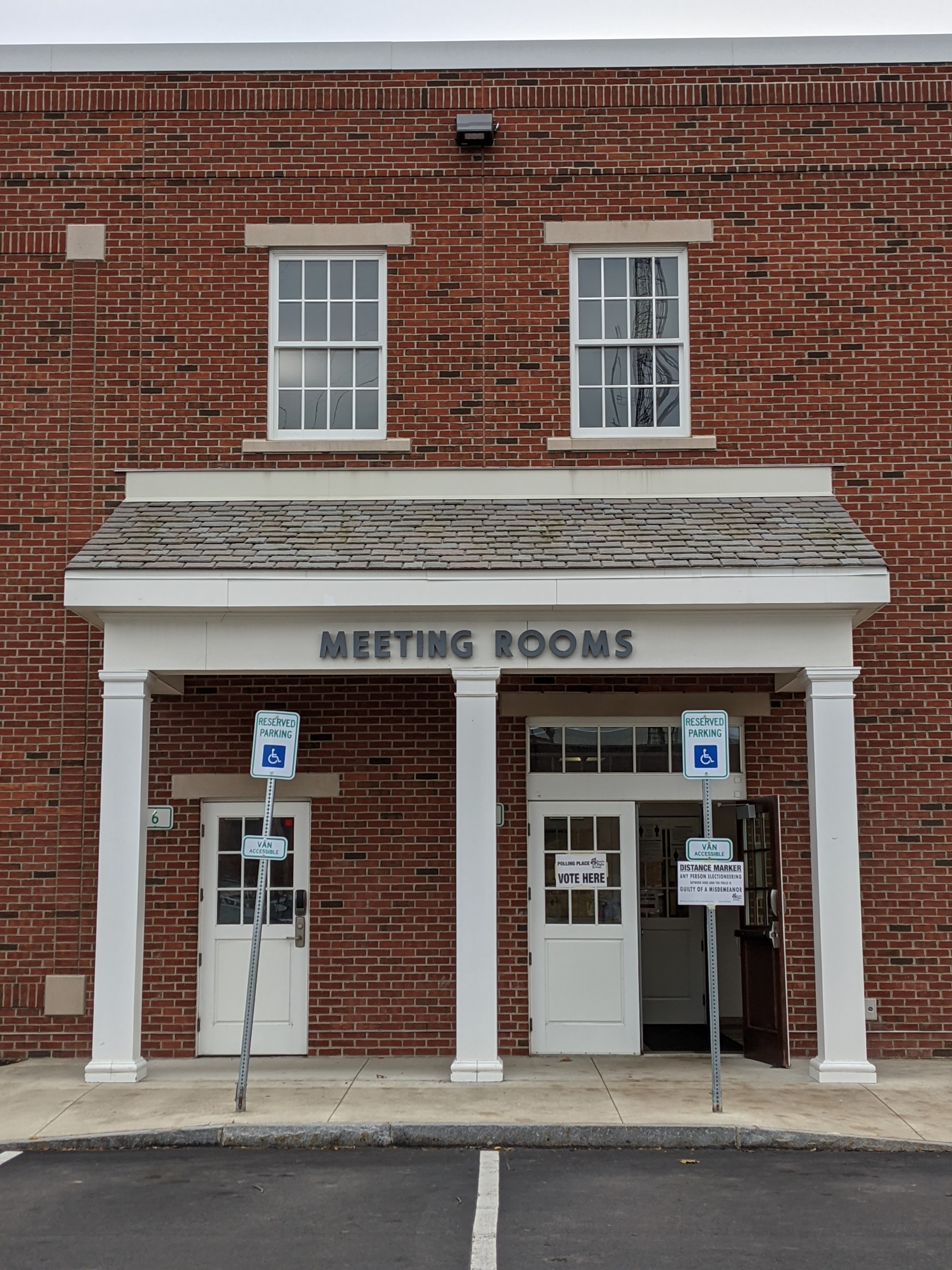 Brick building entrance with 'Vote Here' signs on the doors.