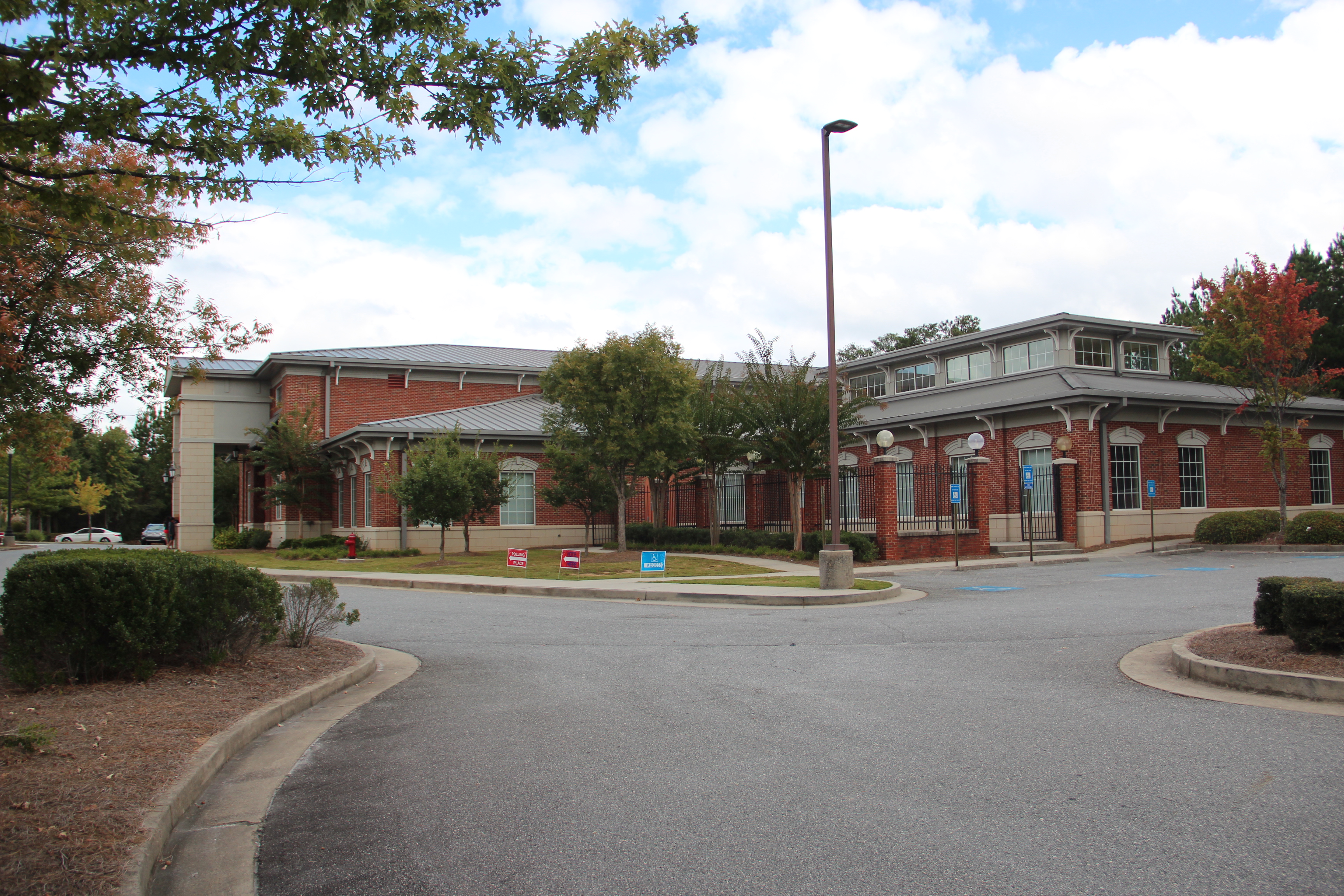 Brick library building with gray metal roof surrounded by trees.