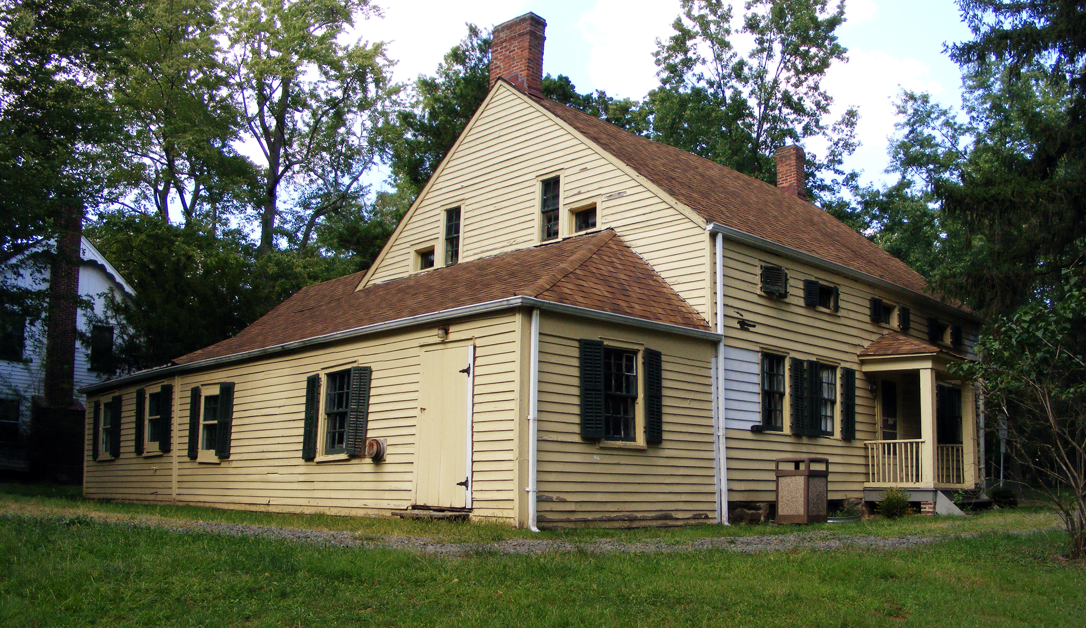 Two-story yellow clapboard colonial farmhouse with brick chimneys and black shutters.