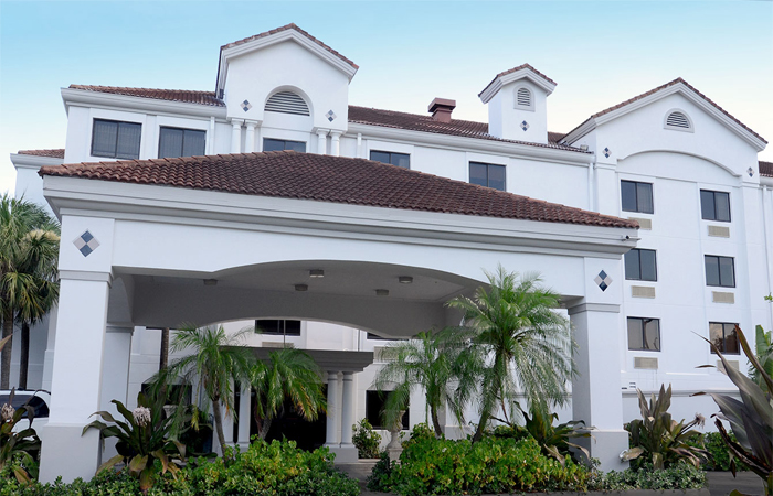 White multi-story building with a covered entrance portico and tropical landscaping.