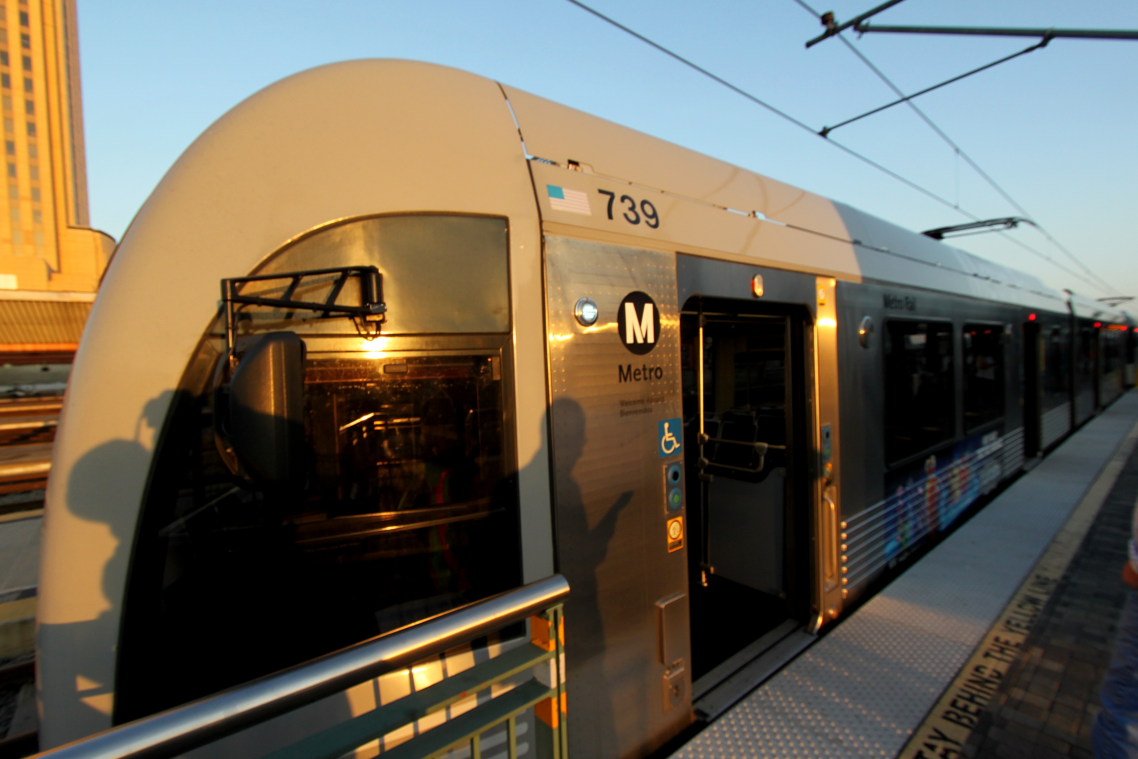 Silver Metro rail car at a station platform with overhead electric wires.