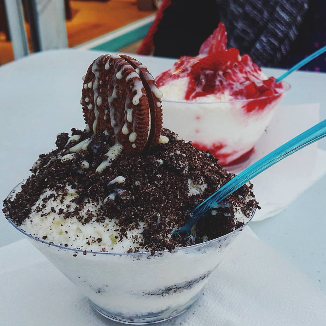 Two cups of Korean shaved ice dessert, one with cookie crumbs and one with strawberry topping.