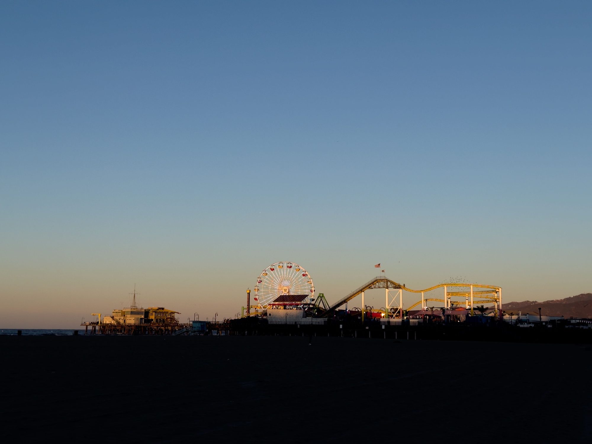 Silhouette of Santa Monica Pier featuring a Ferris wheel during a serene sunset in California.
