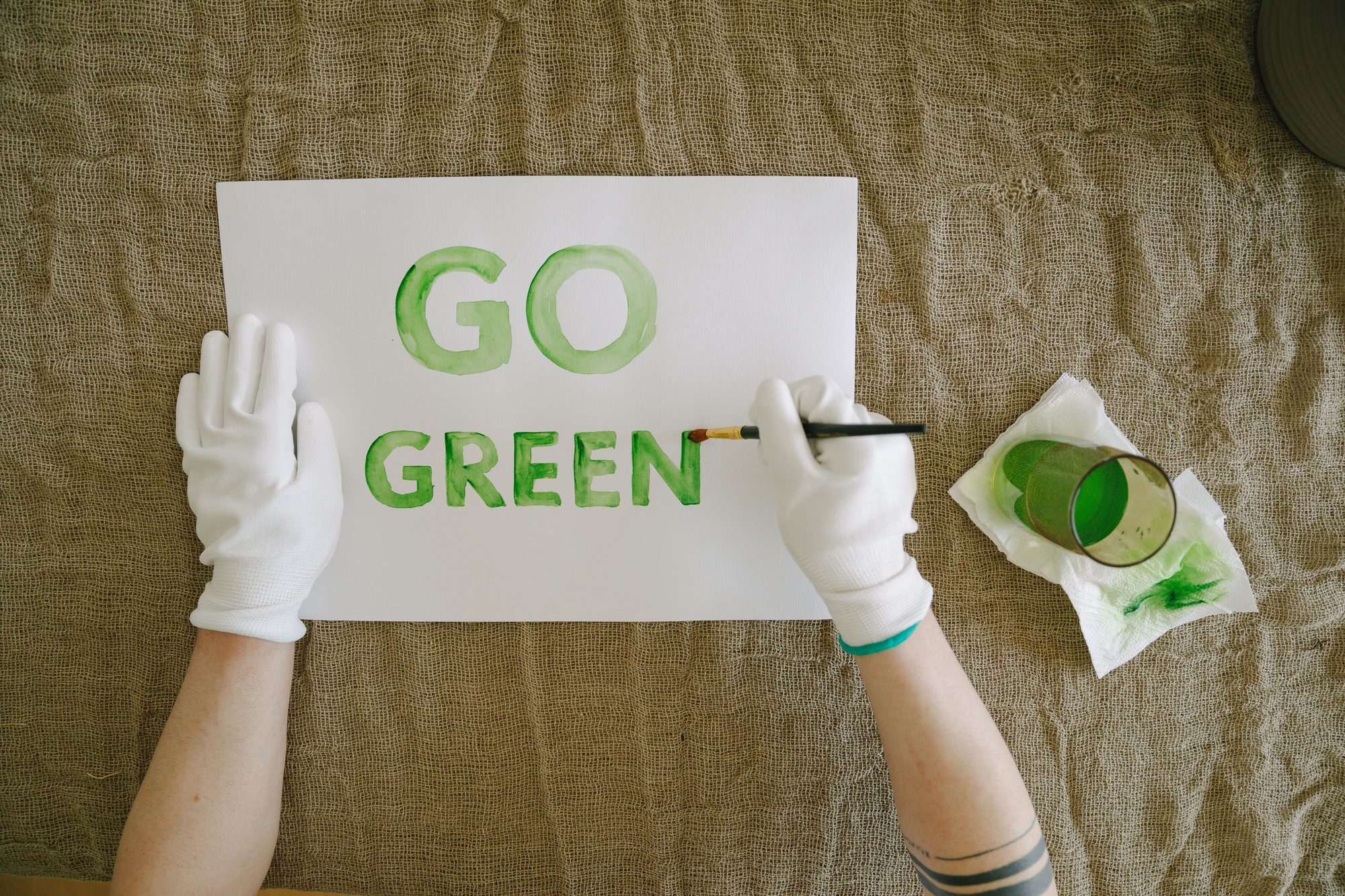 Overhead view of go green poster creation with paint and gloves on natural fabric background.