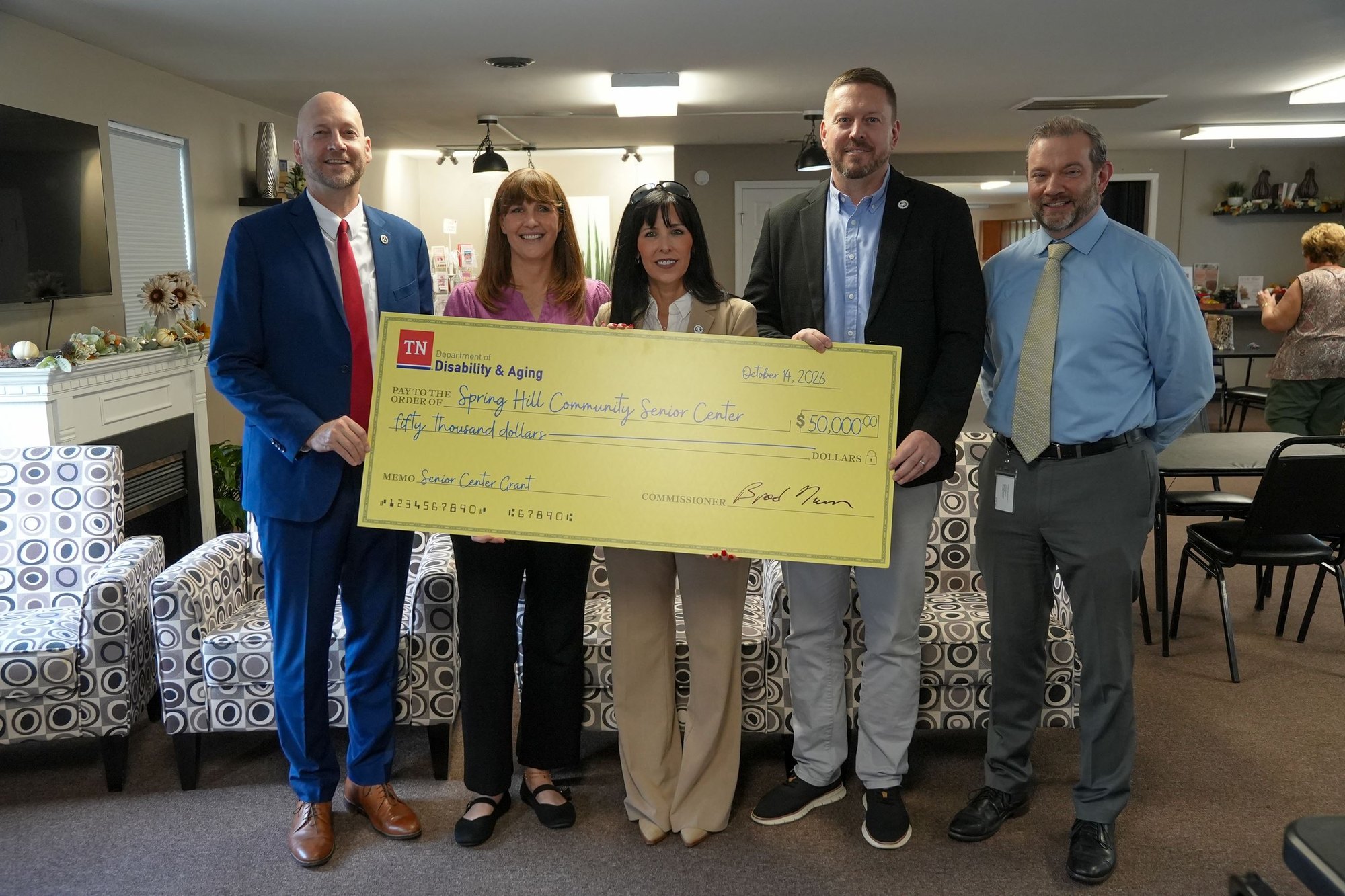 Five adults indoors holding a large ceremonial check inside a community center.